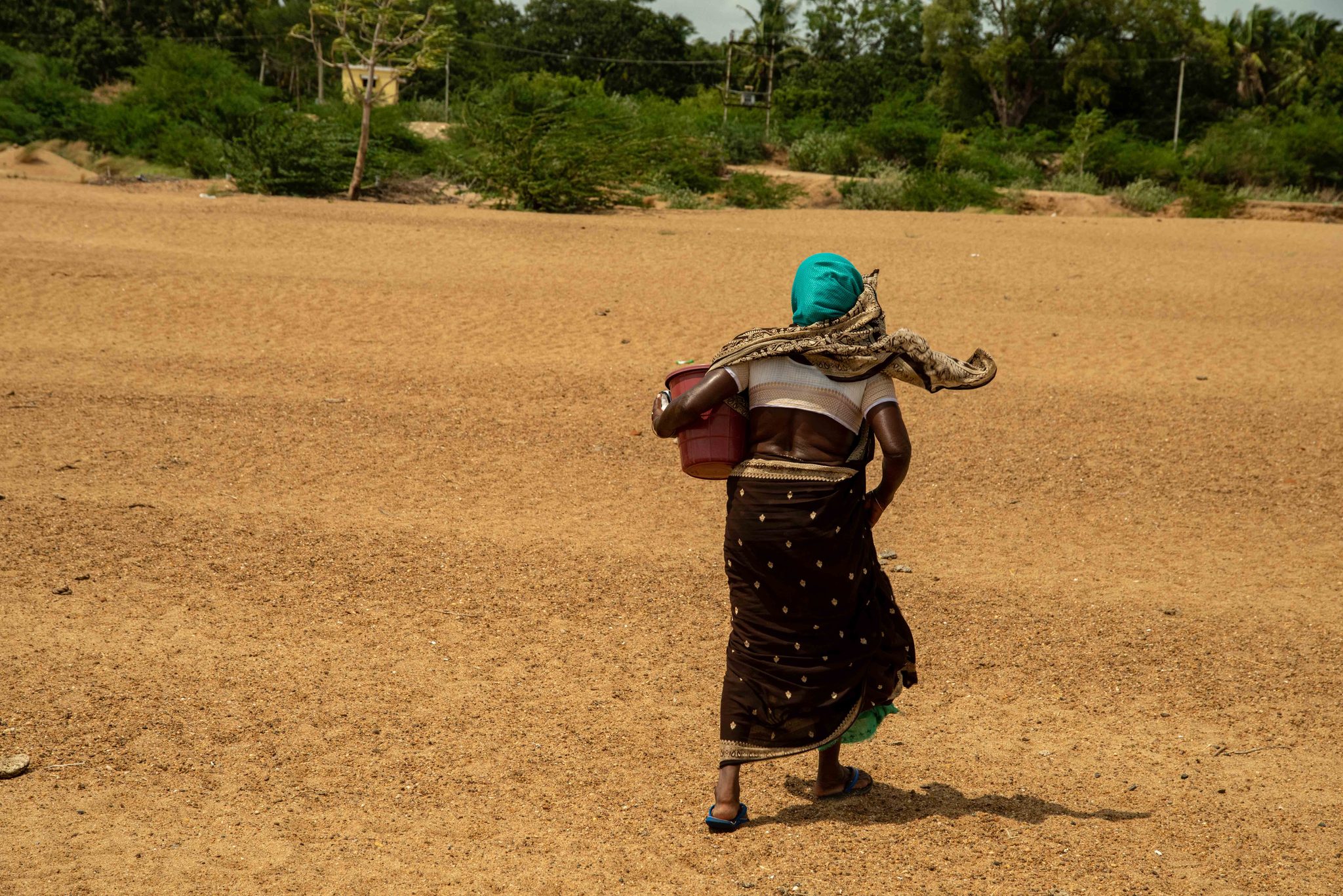 Bucket in hand, she crosses the wide sand toward the trees.