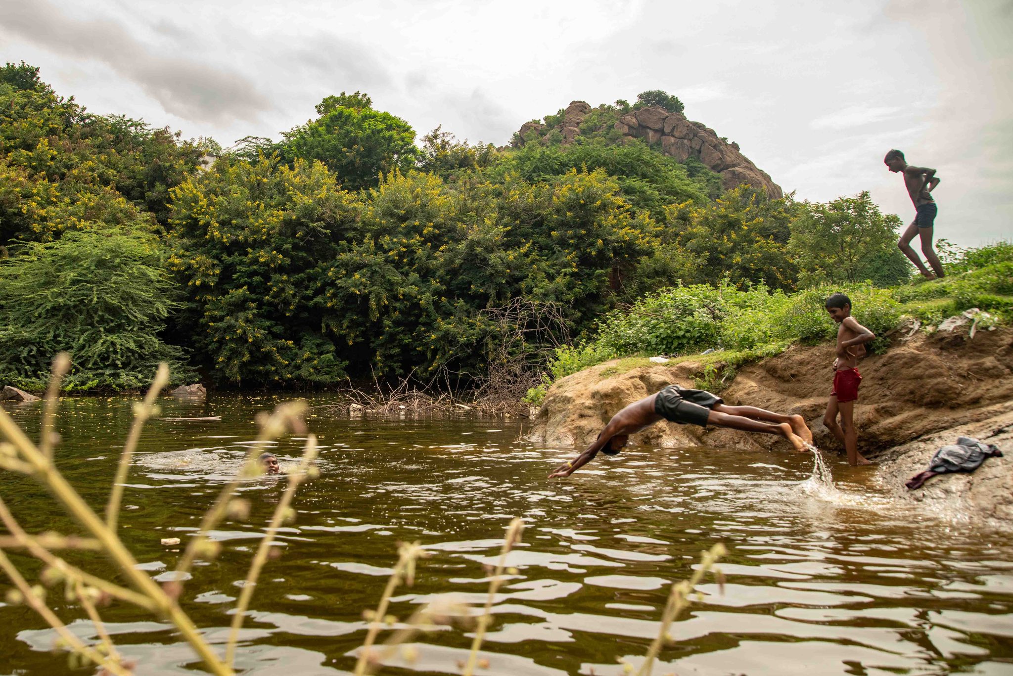 One boy hits the water as another climbs the rock for his turn.