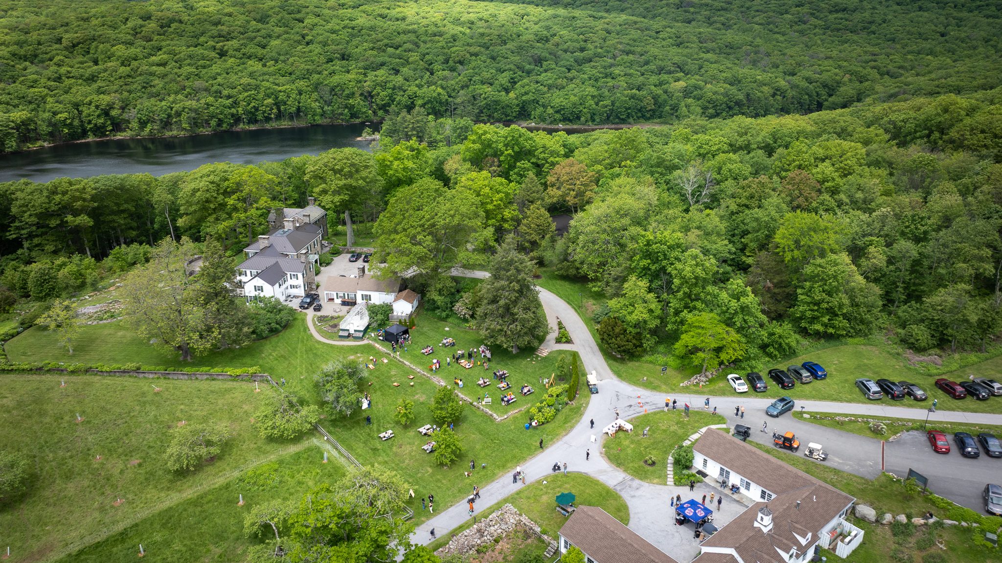 The main house and its lawn fill with visitors, the lake just past the tree line.