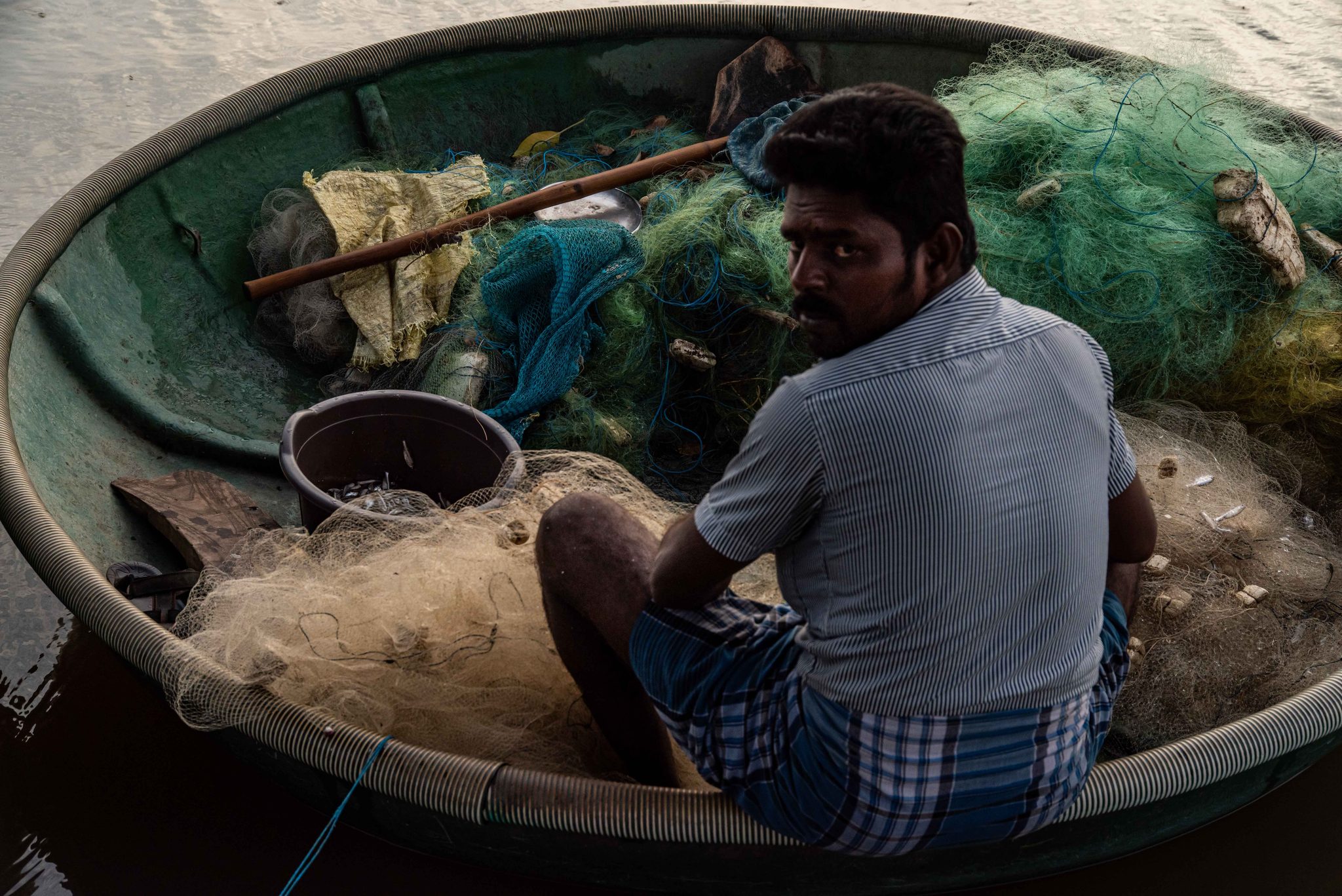 He glances up from the net, the coracle heaped with green mesh.
