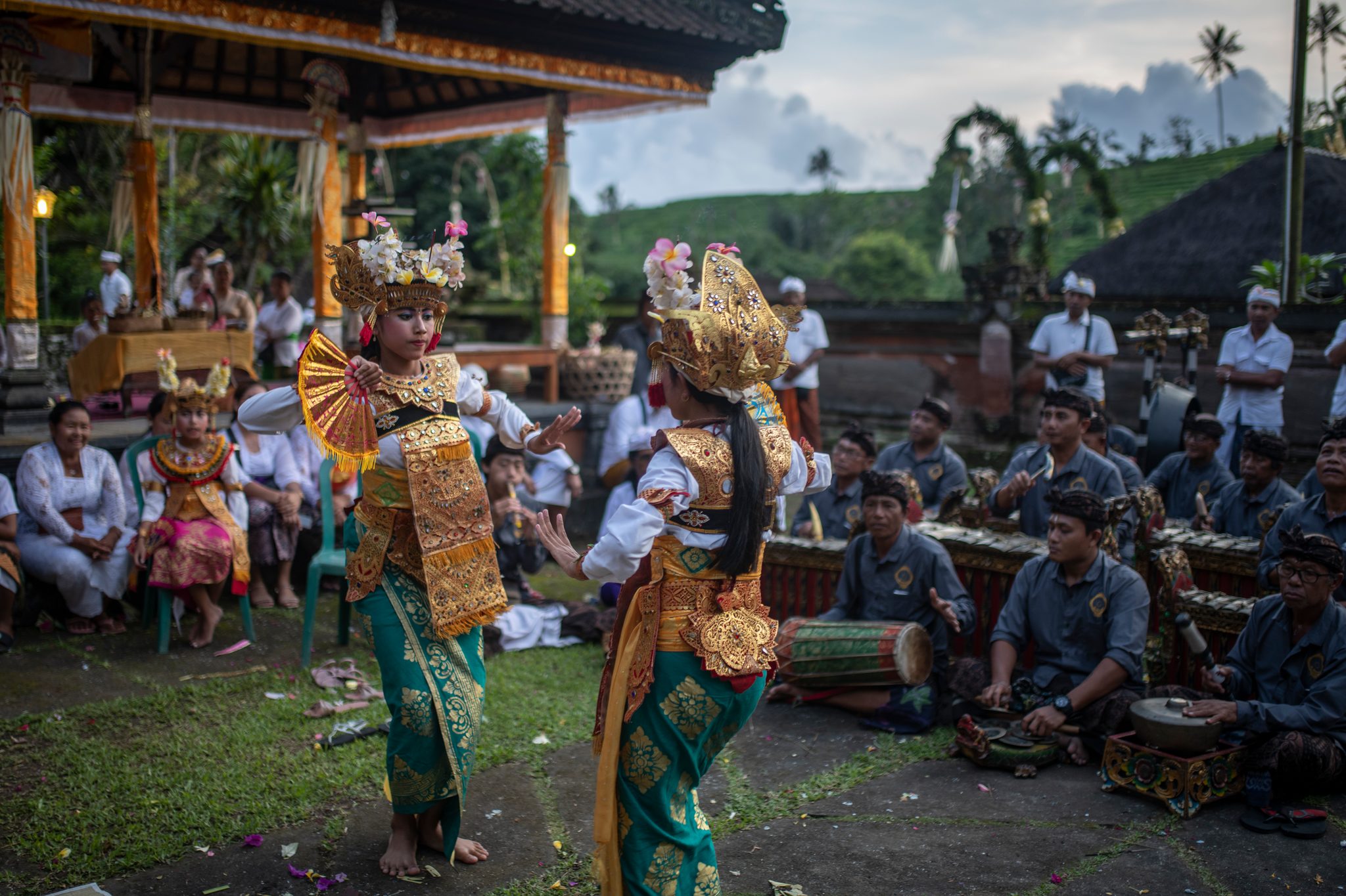 Two young dancers in gold move to the gamelan while the temple courtyard looks on.