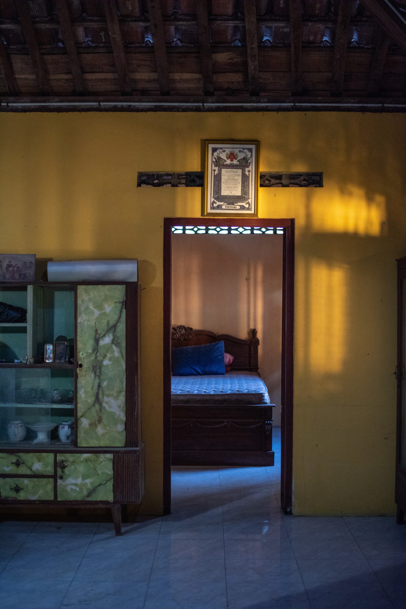 Inside the house, lamplight falls across the yellow walls and into the bedroom beyond.