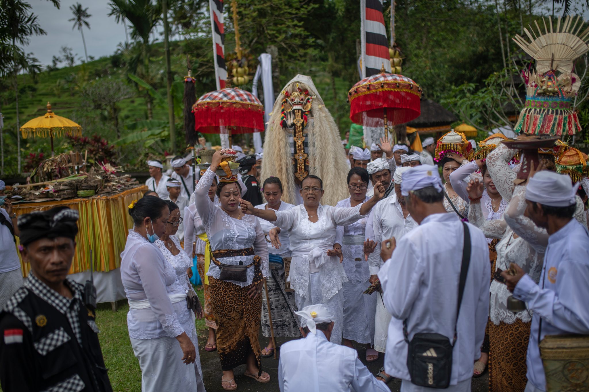 A woman in white dances at the center of the crowd, arms flung wide, while the masked figure looks on.