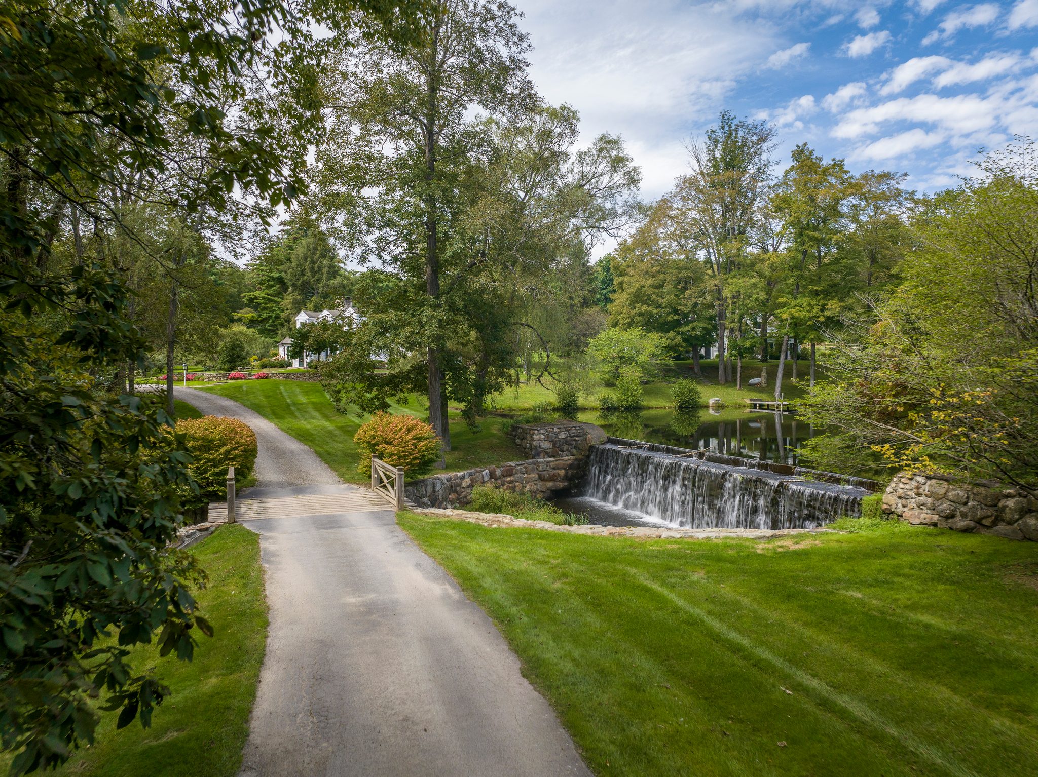 A gravel drive bends past a stone spillway where the stream drops in a white sheet in mid-September.