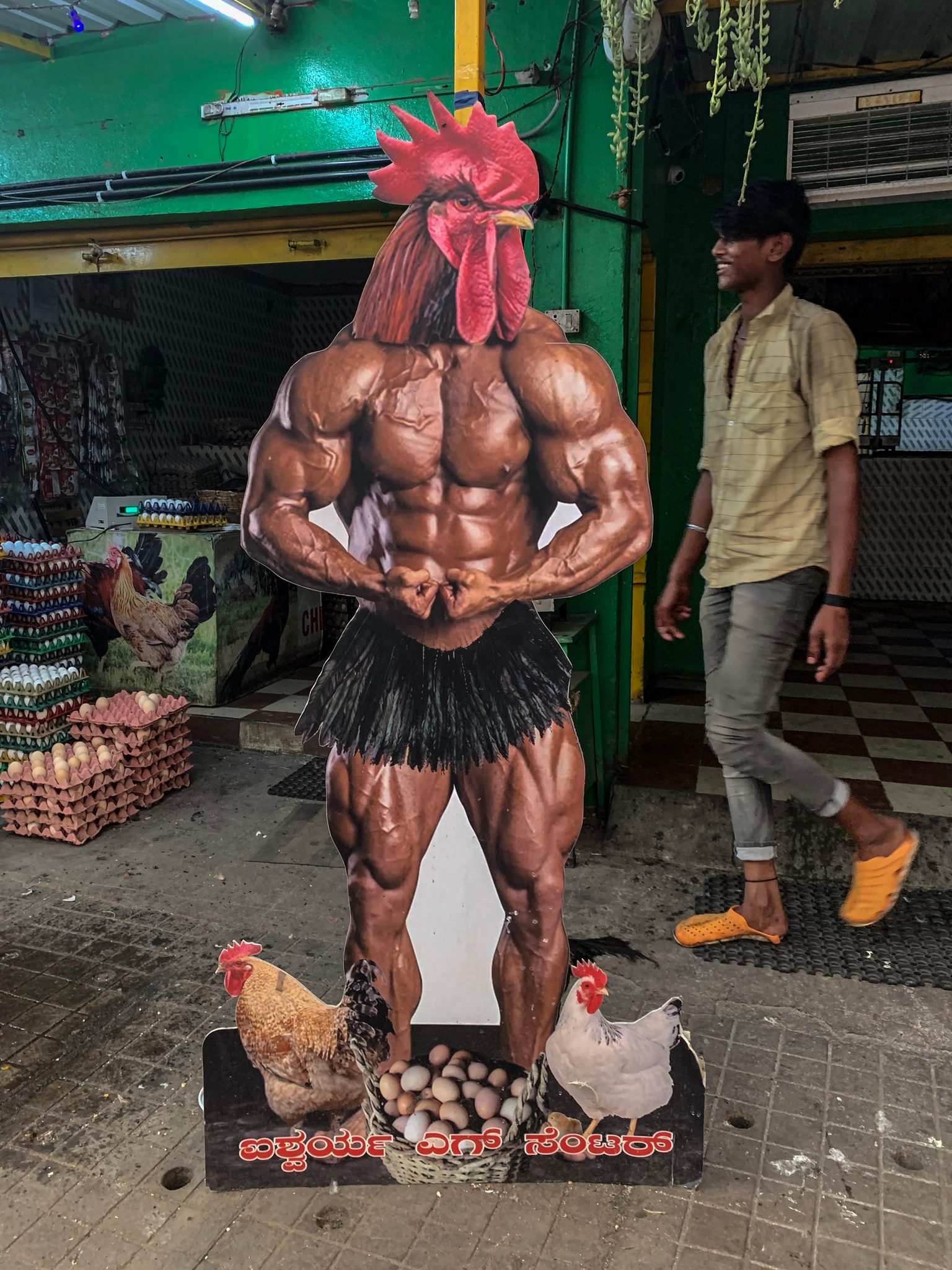 A cutout of a muscle-bound rooster flexes outside the egg shop while a man laughs as he walks by.