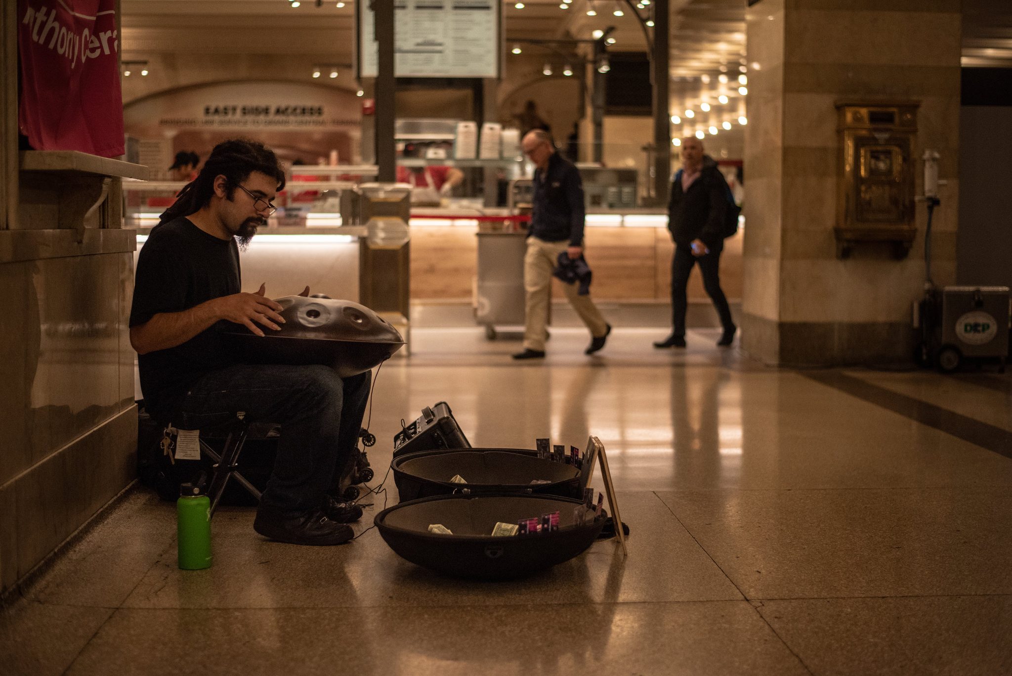 Anthony plays the hand pan as commuters stride past the food counters.