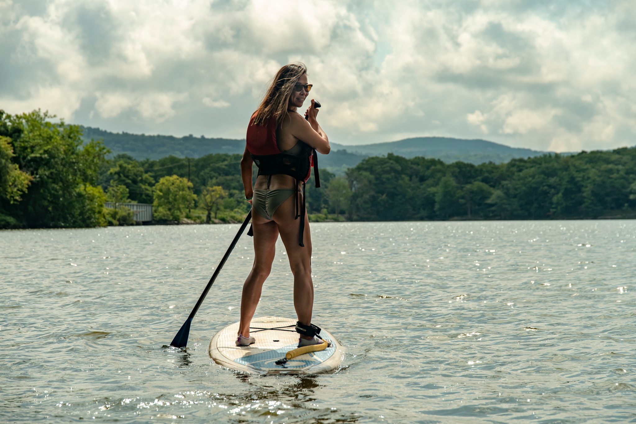 A paddleboarder finds her balance on the open water, green hills on every side.