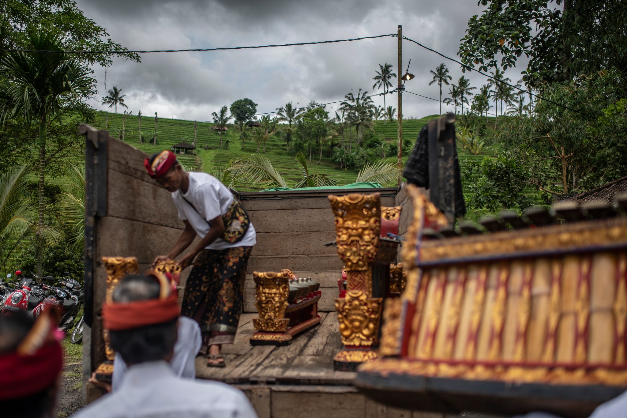 Gilded gamelan frames come off the back of a truck, rice terraces rising behind them.