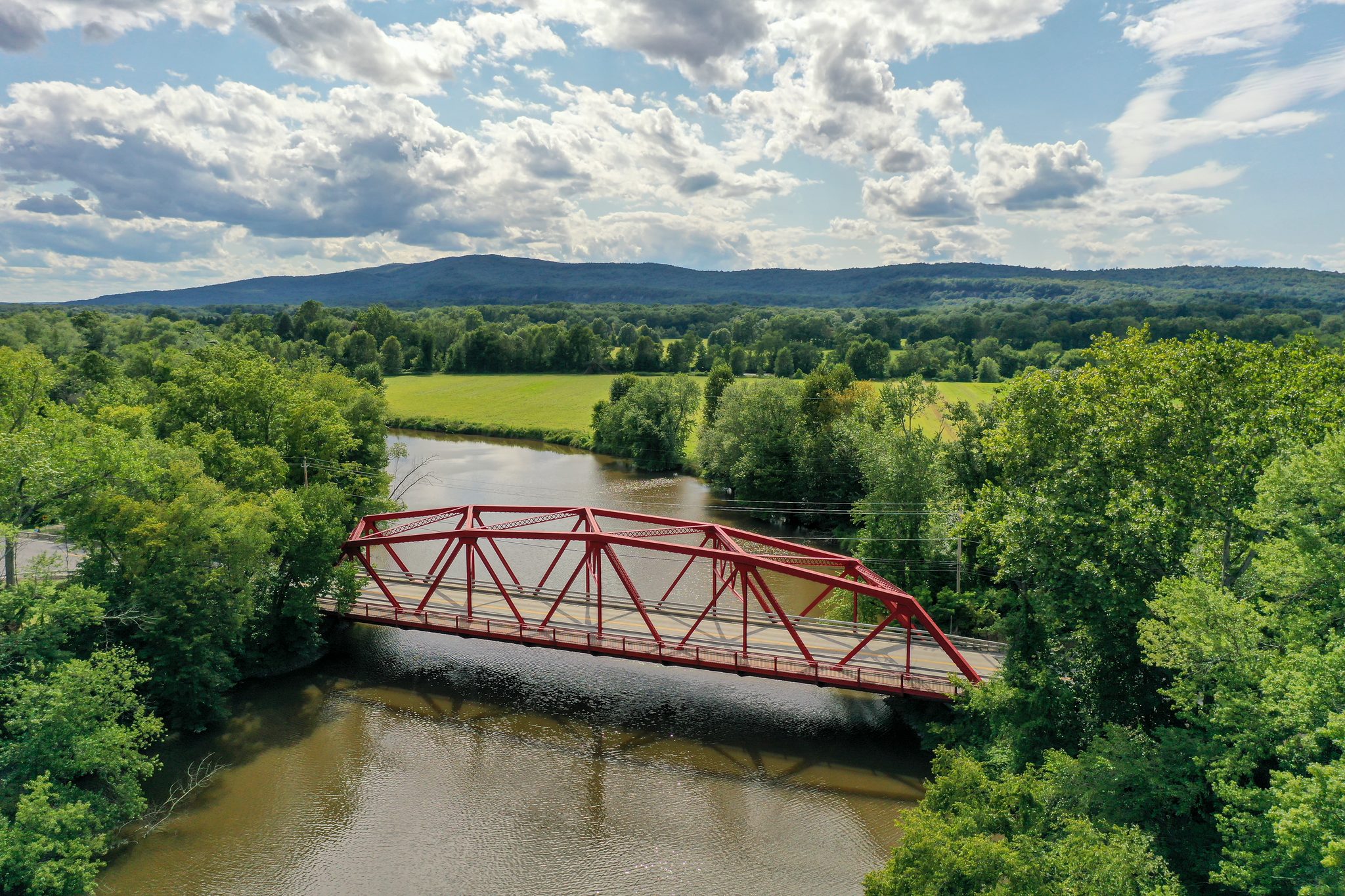 A red truss bridge spans the river between fields and forest, the hills rolling away to the horizon.