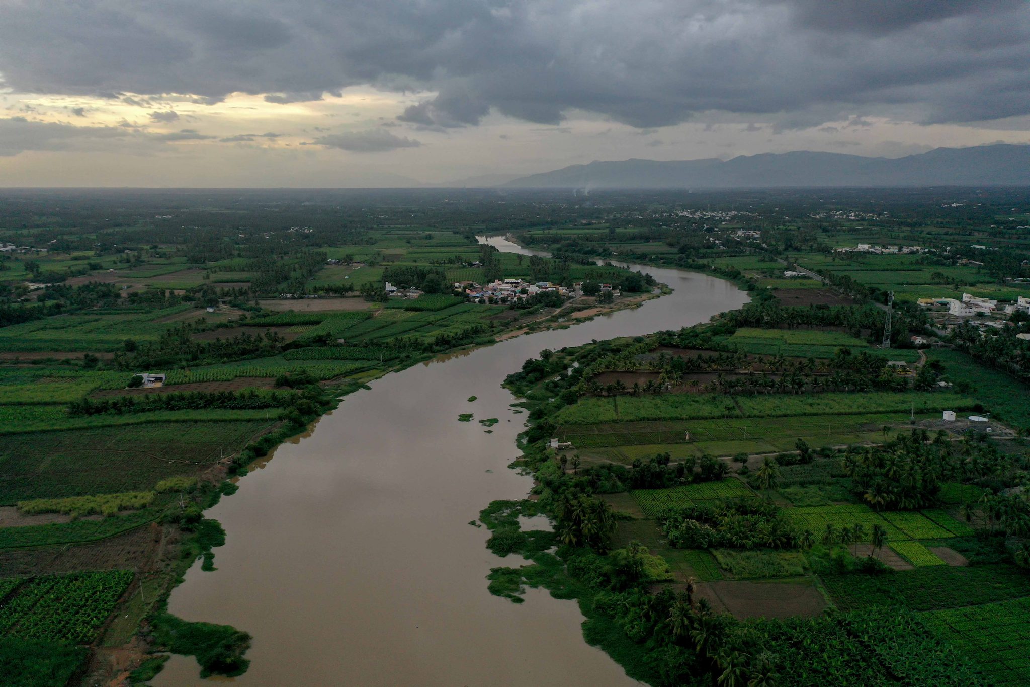 The river bends through green farmland beneath a stormy sky.