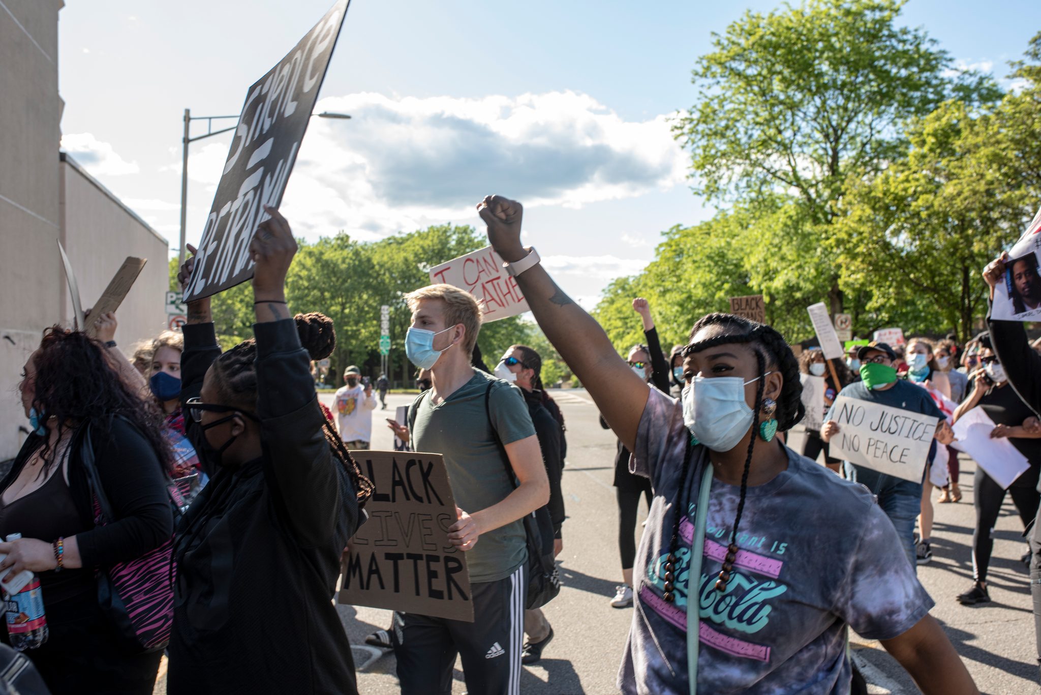 Fists go up as the march turns the corner, a sign reading No Justice No Peace held just behind.