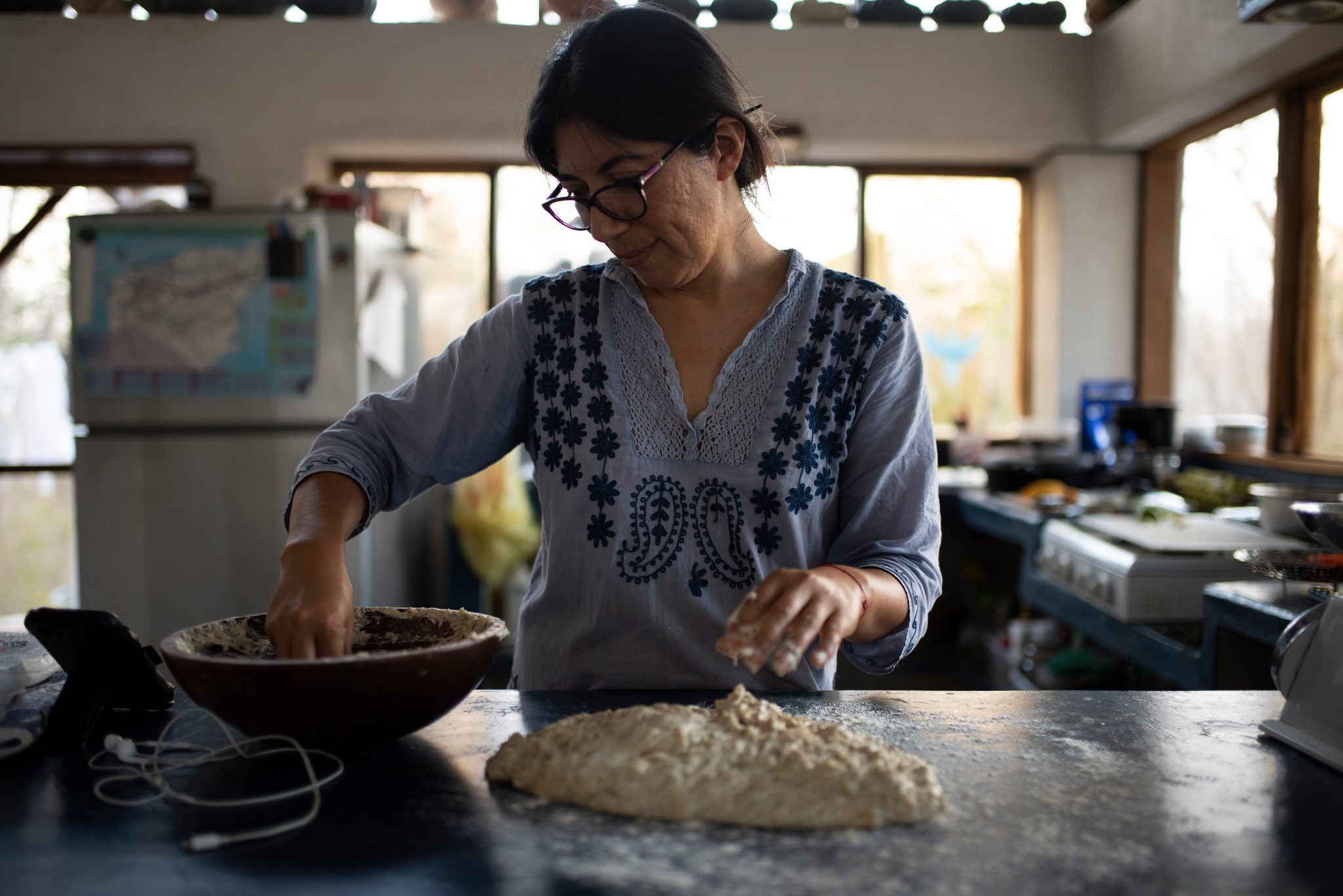 She works the dough in a wooden bowl on the kitchen counter.