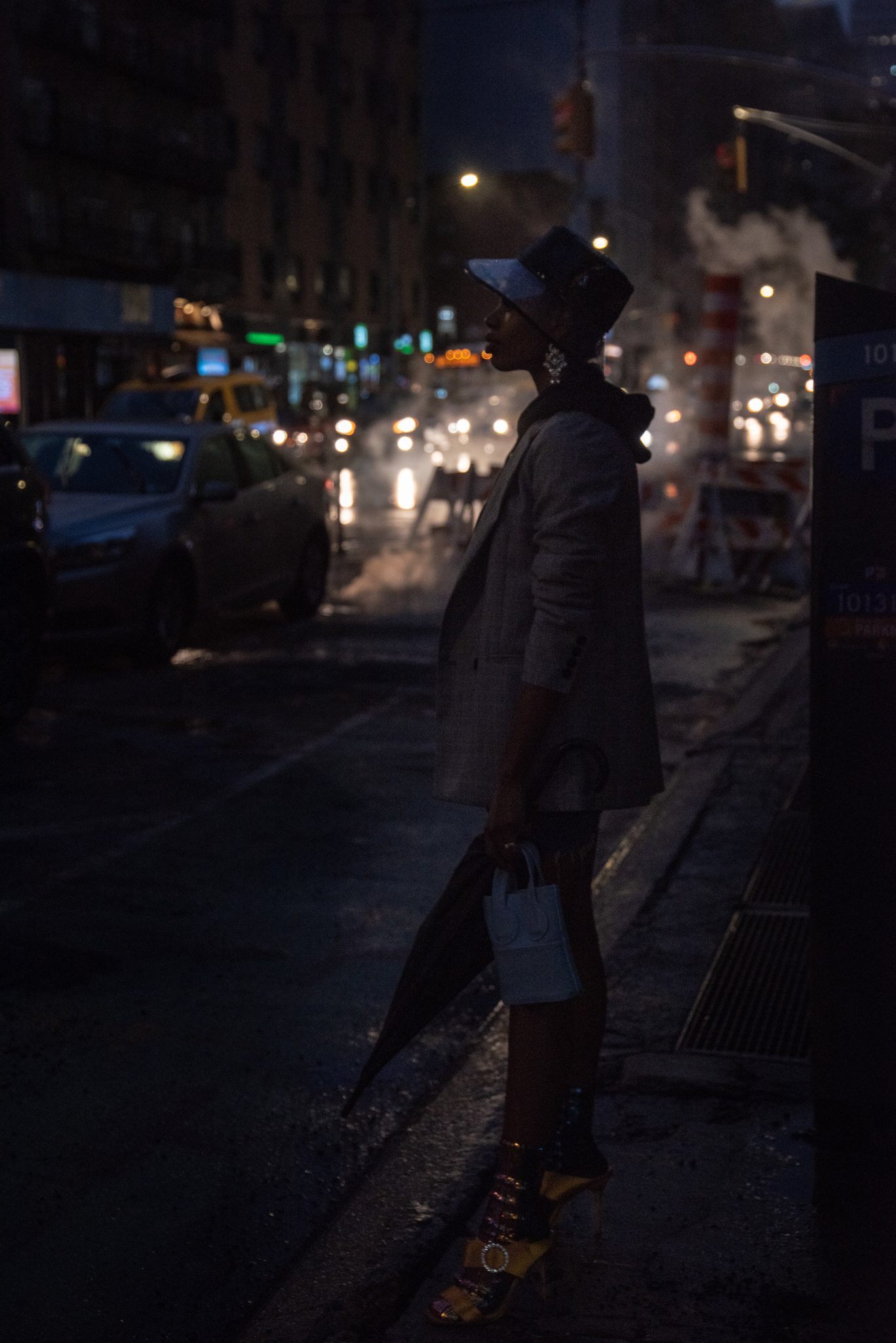 She stands at the curb in a wide-brimmed hat, the steam rising behind her.