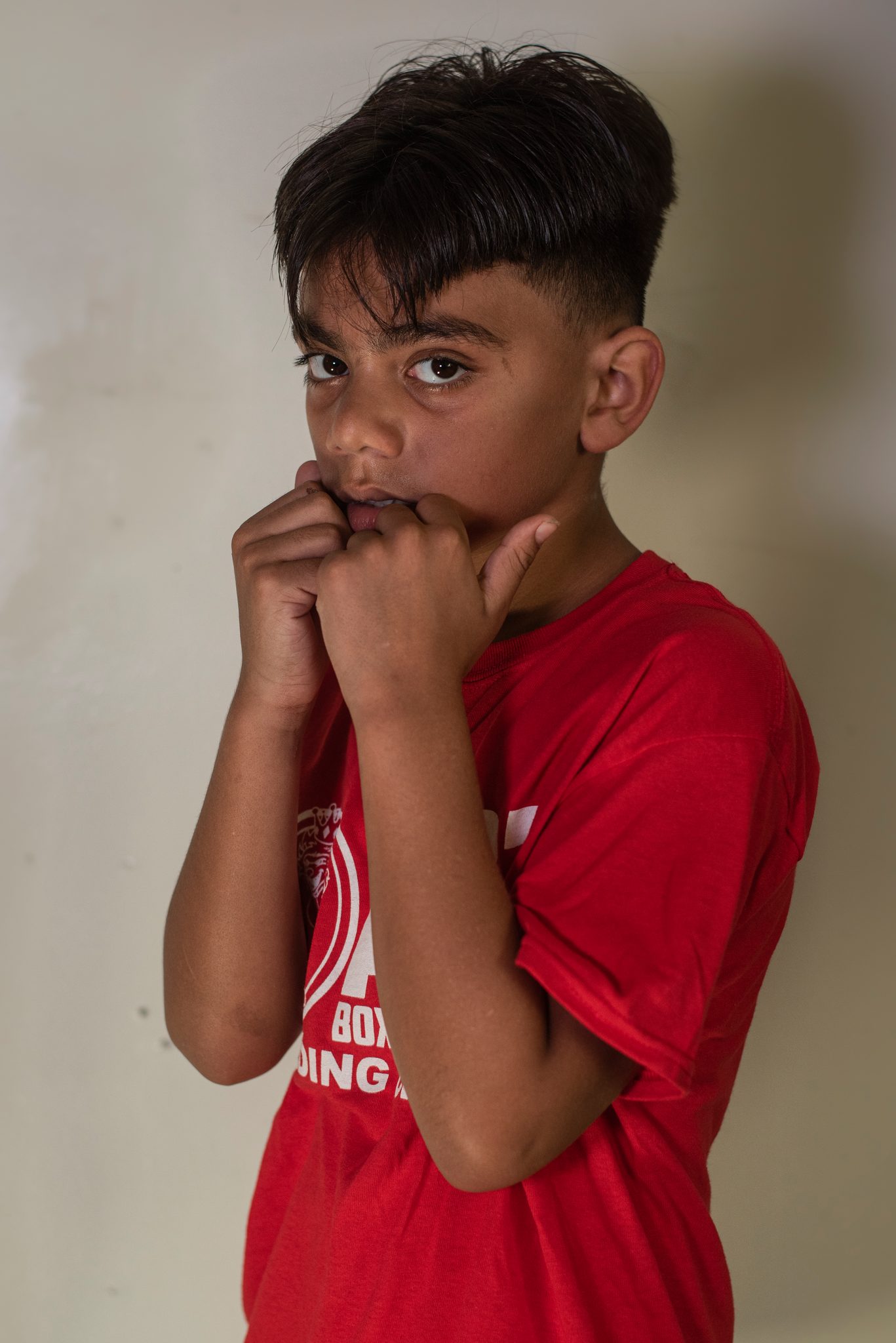 The same boy turns sideways and presses his fists to his mouth, eyes steady over his knuckles.