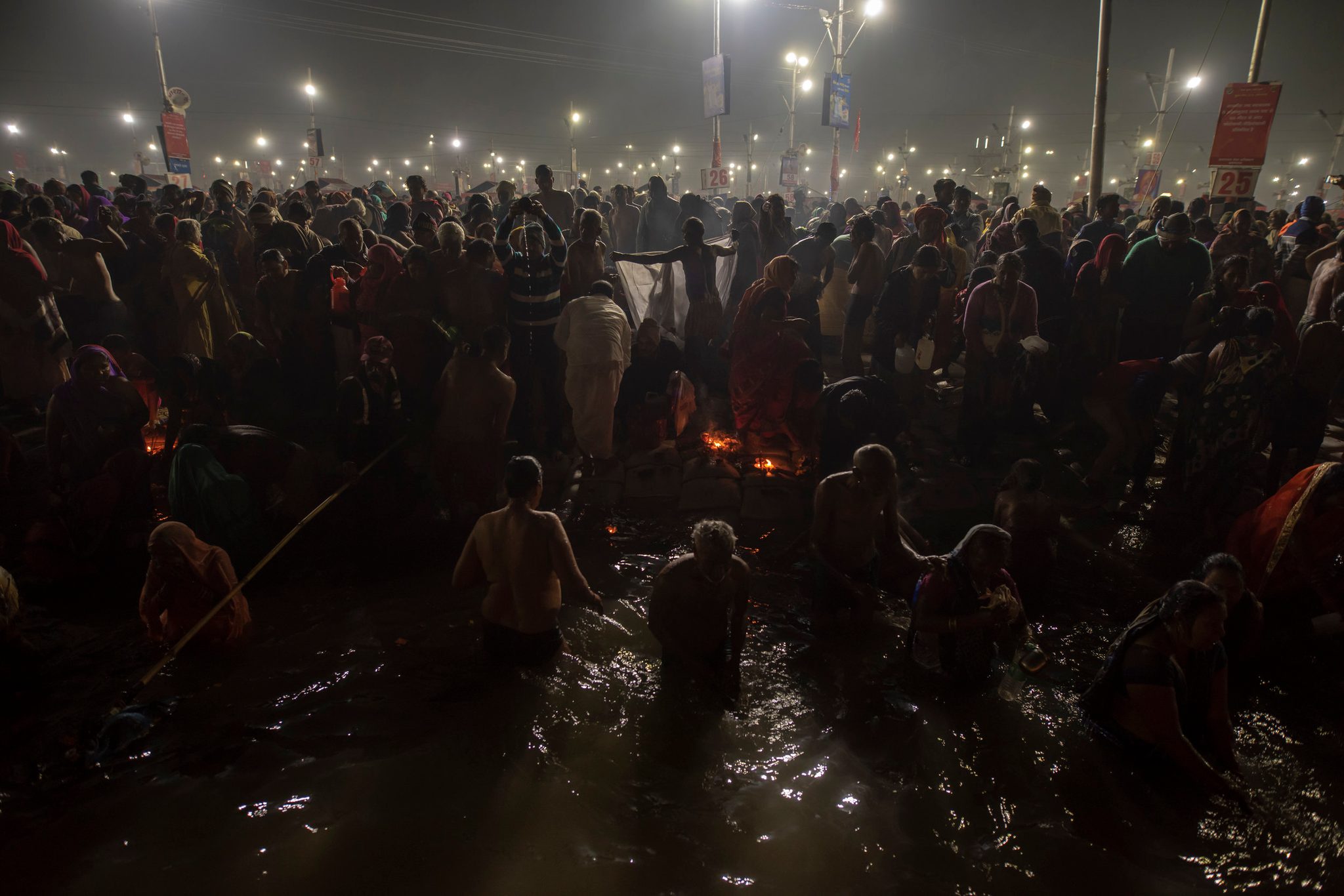 Under the floodlights, pilgrims wade into the river in the dark before dawn.