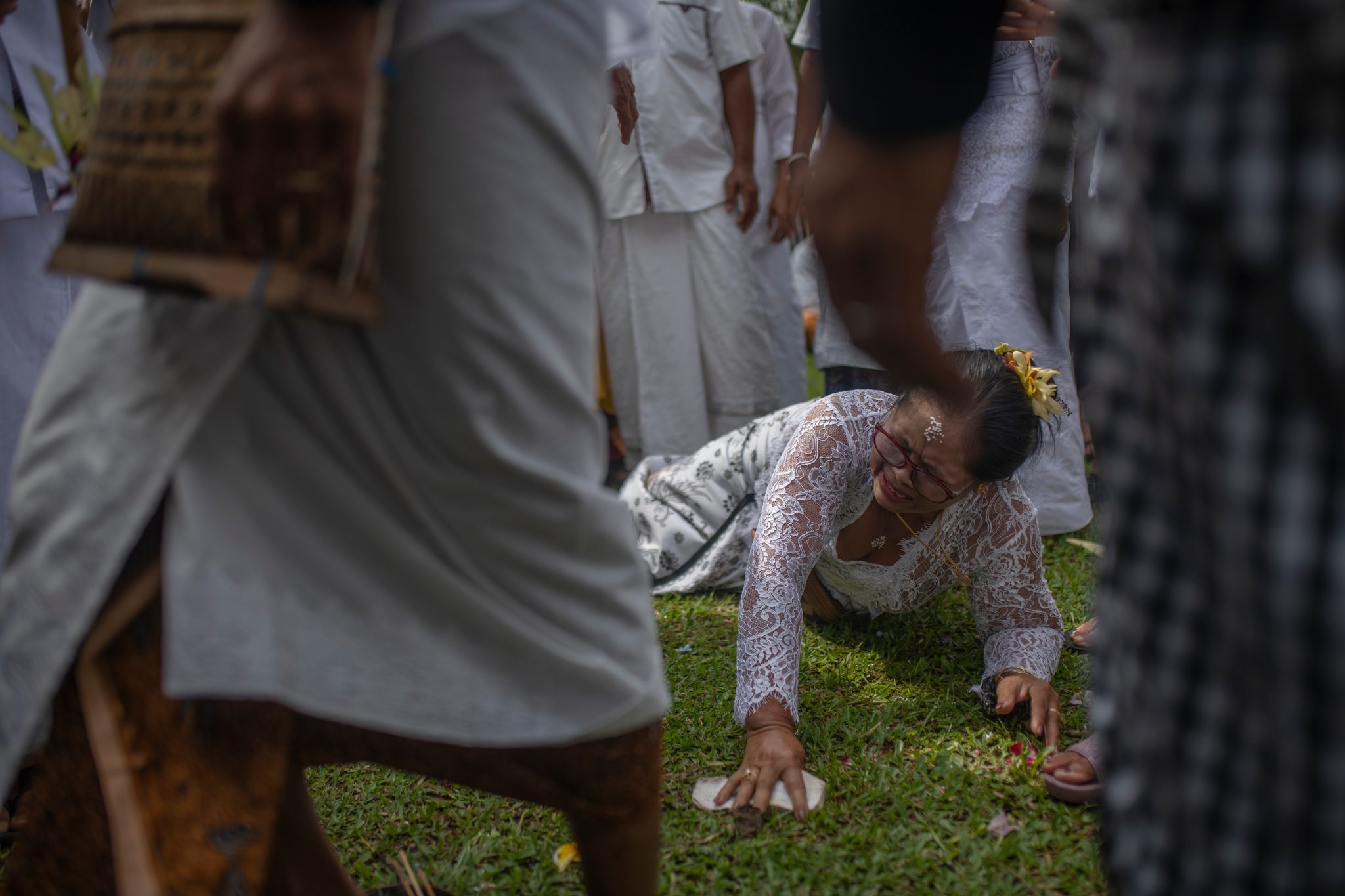 A woman sinks to the grass in the middle of the ceremony, hands pressed to the earth, as the crowd moves around her.