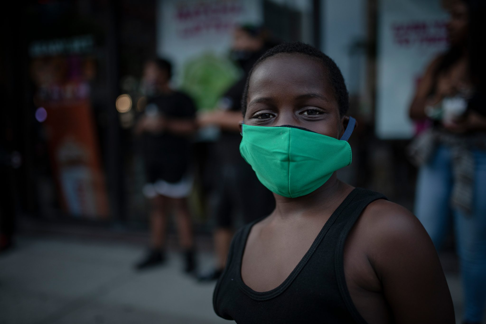 On Juneteenth, a woman in a green mask stands in the evening street as the march gathers.