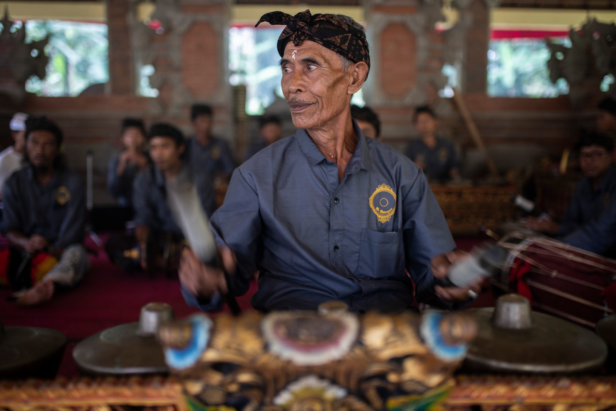An elder of the gamelan plays without looking down, his eyes on something across the pavilion.
