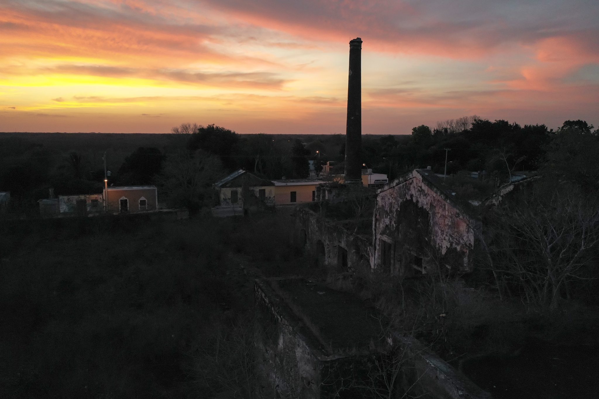 An old chimney stands against a blazing sunset over the rooftops.