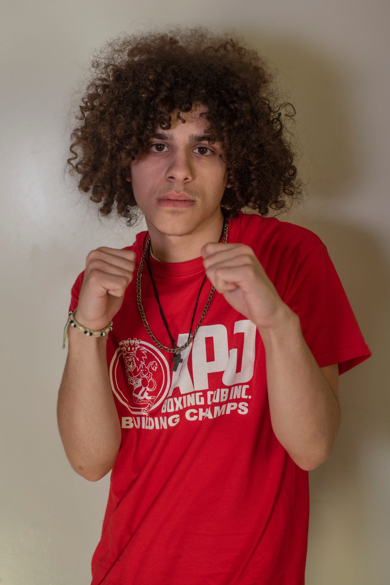 A teenager with a halo of curls raises his fists, a cross on a cord and a bracelet at his wrist.