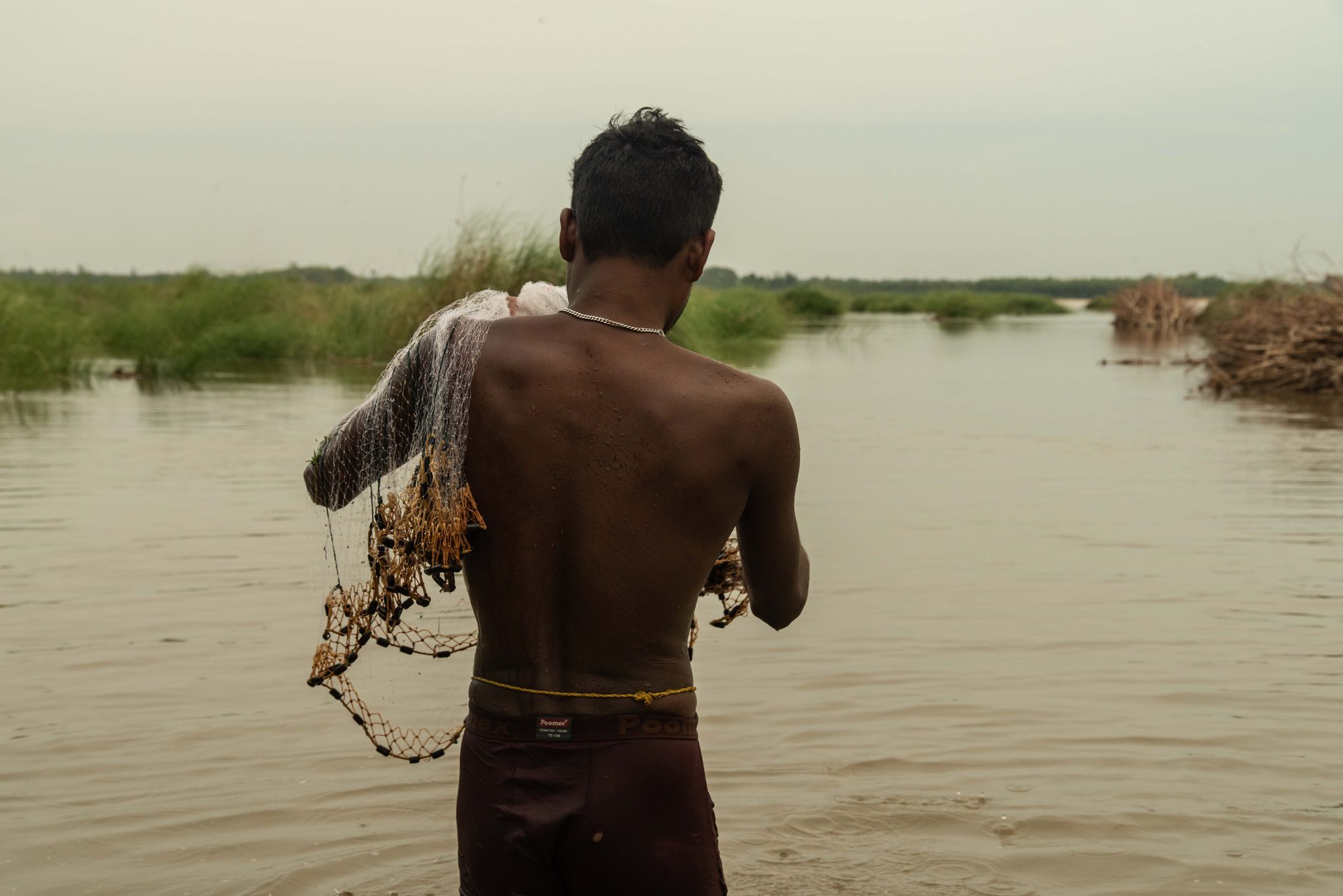 A fisherman wades out with his net over his shoulder.