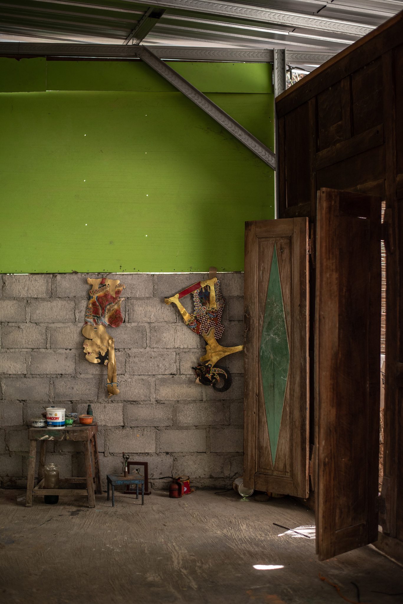 Two puppets hang on the bare wall of an empty room, the door left open.