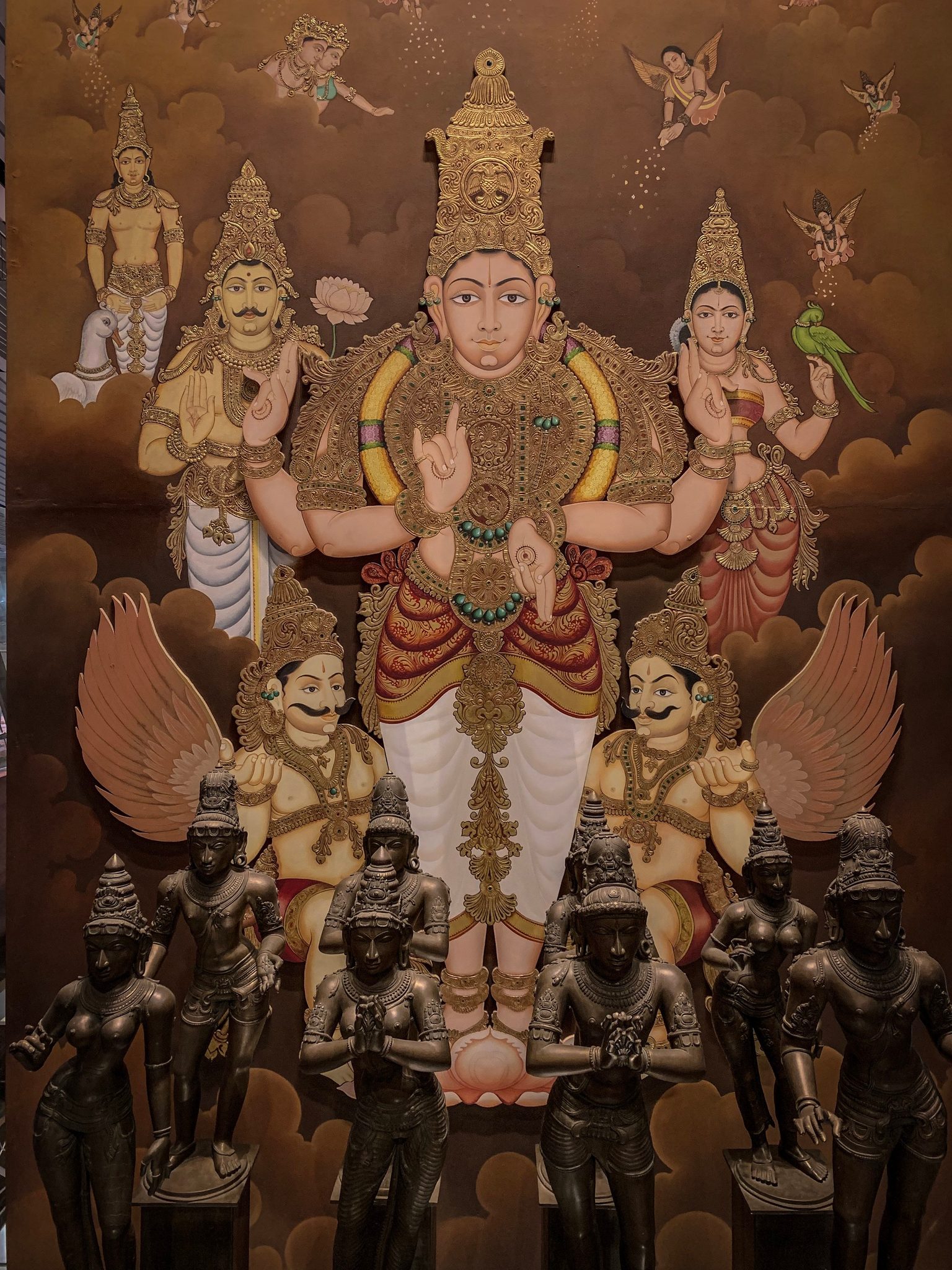 A painted deity sits among the gods, bronze figures lined up at its feet.