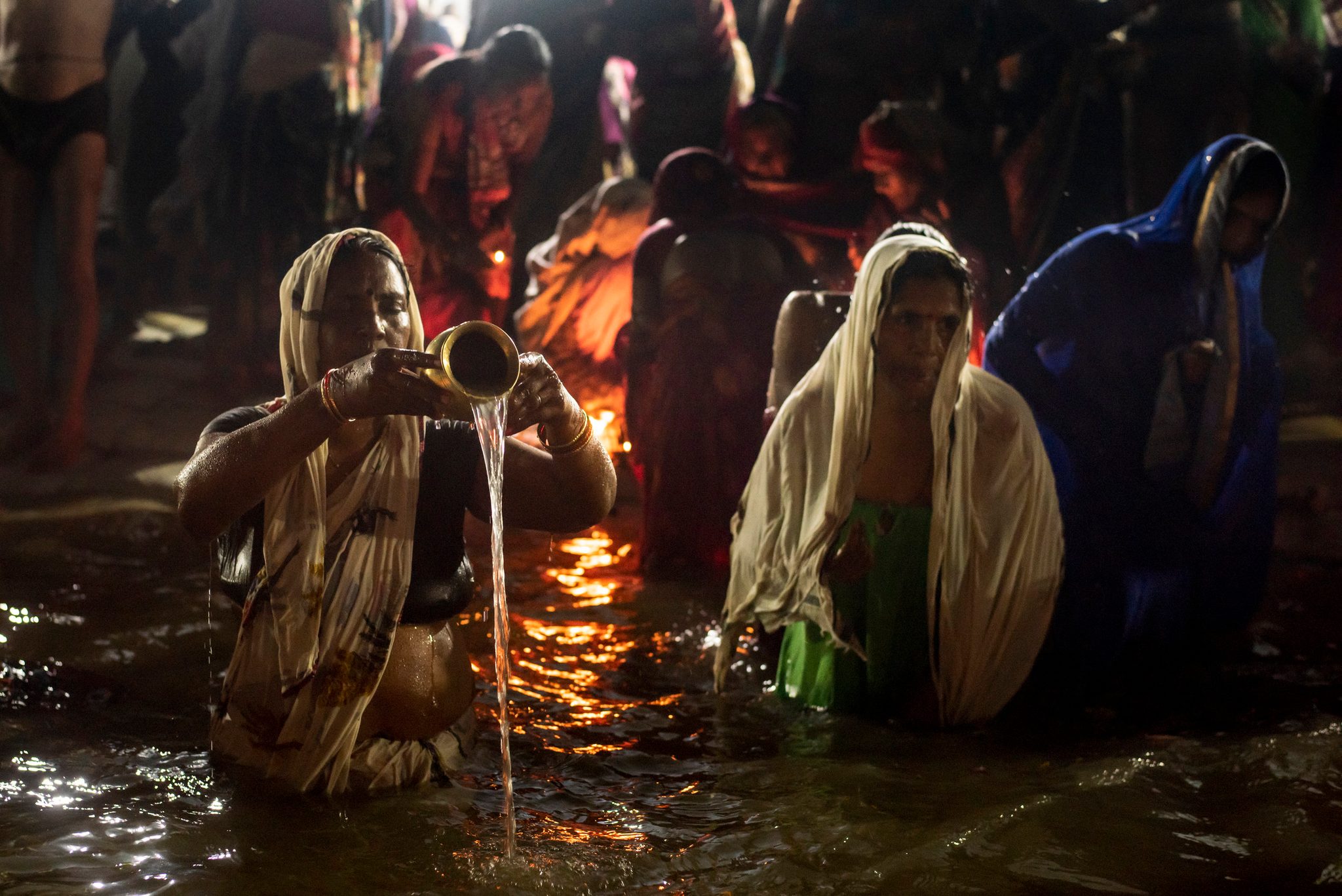 Women gather at the shores of the ganges, pouring water from lota pots, lighting puja offerings and performing ablutions