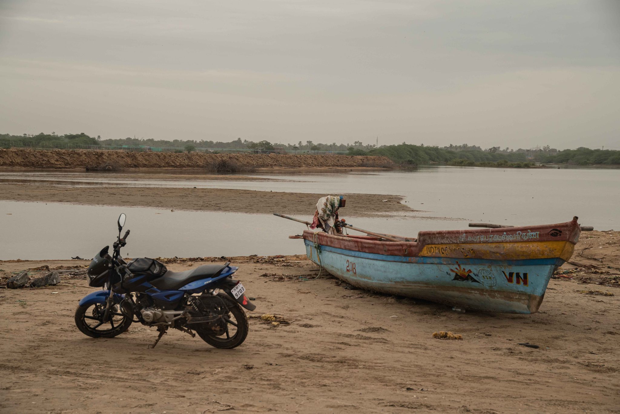 A motorbike waits beside a boat pulled up on the riverbank.