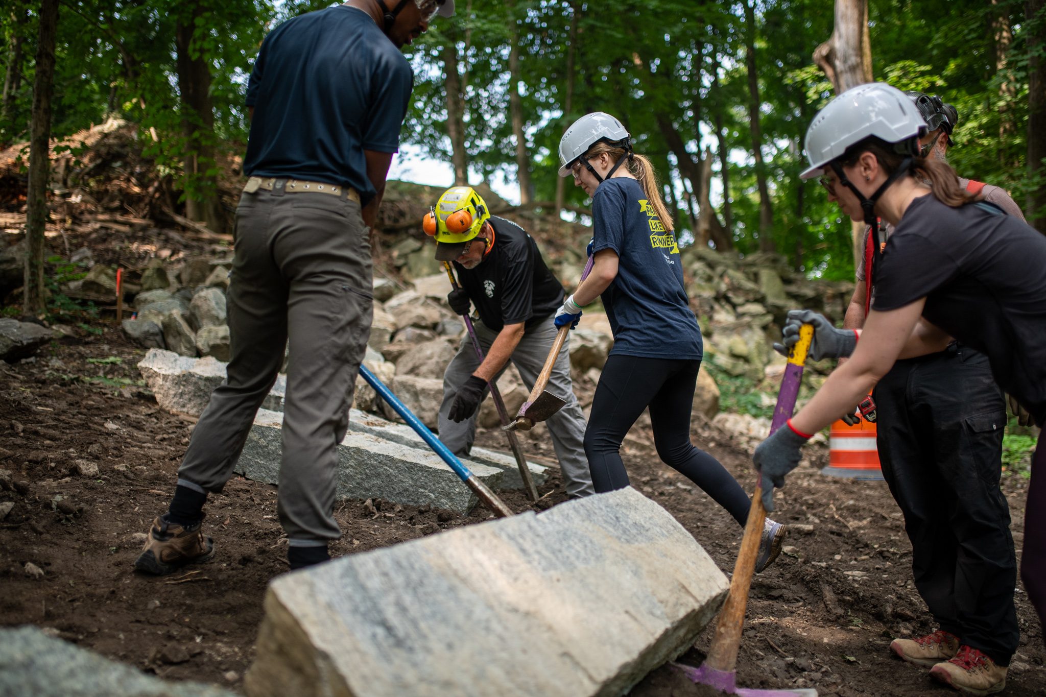 Four crew members lean into their bars to shift a granite block.