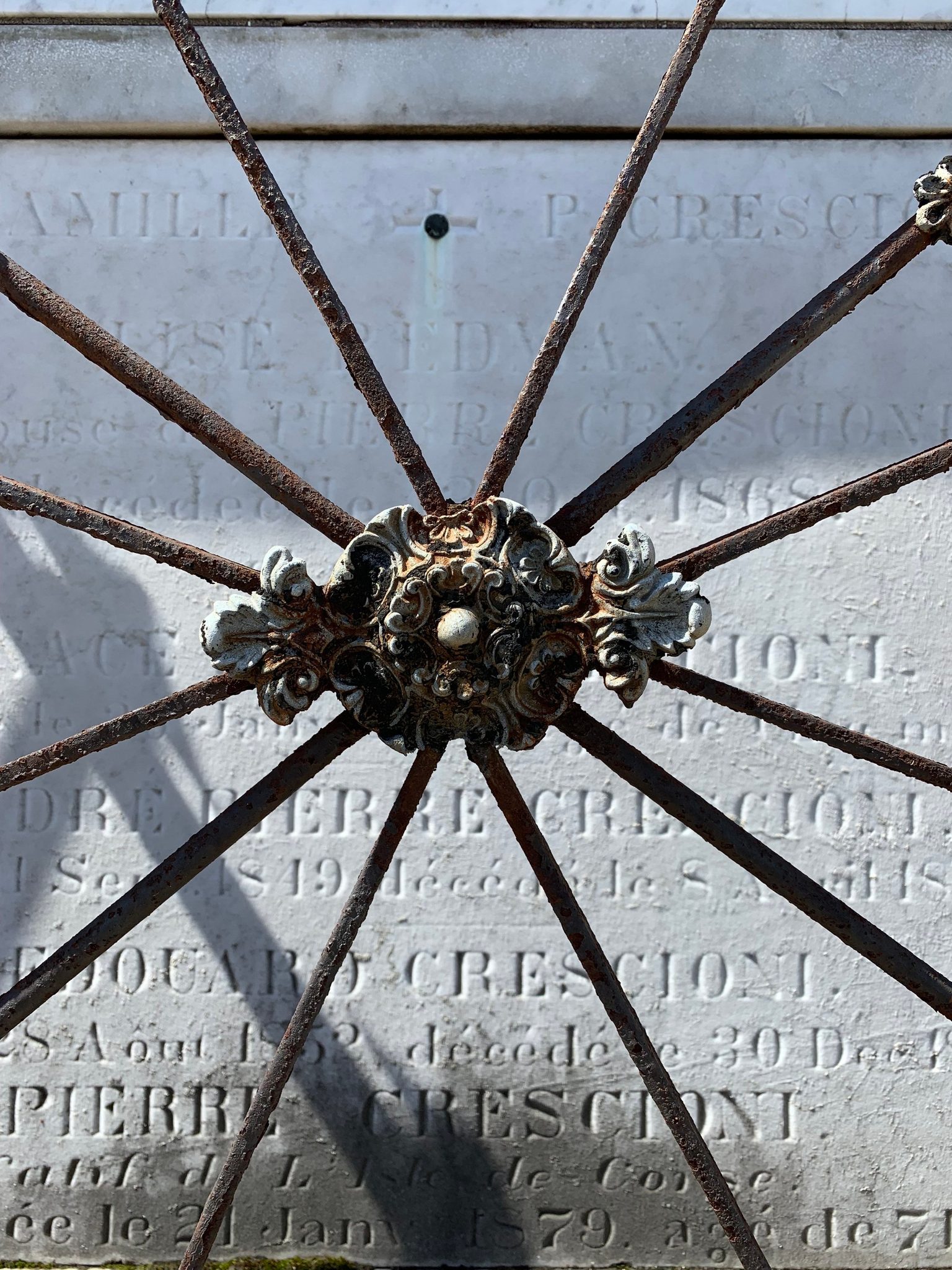 An iron wheel leans against a marble tomb, its French inscriptions worn soft.