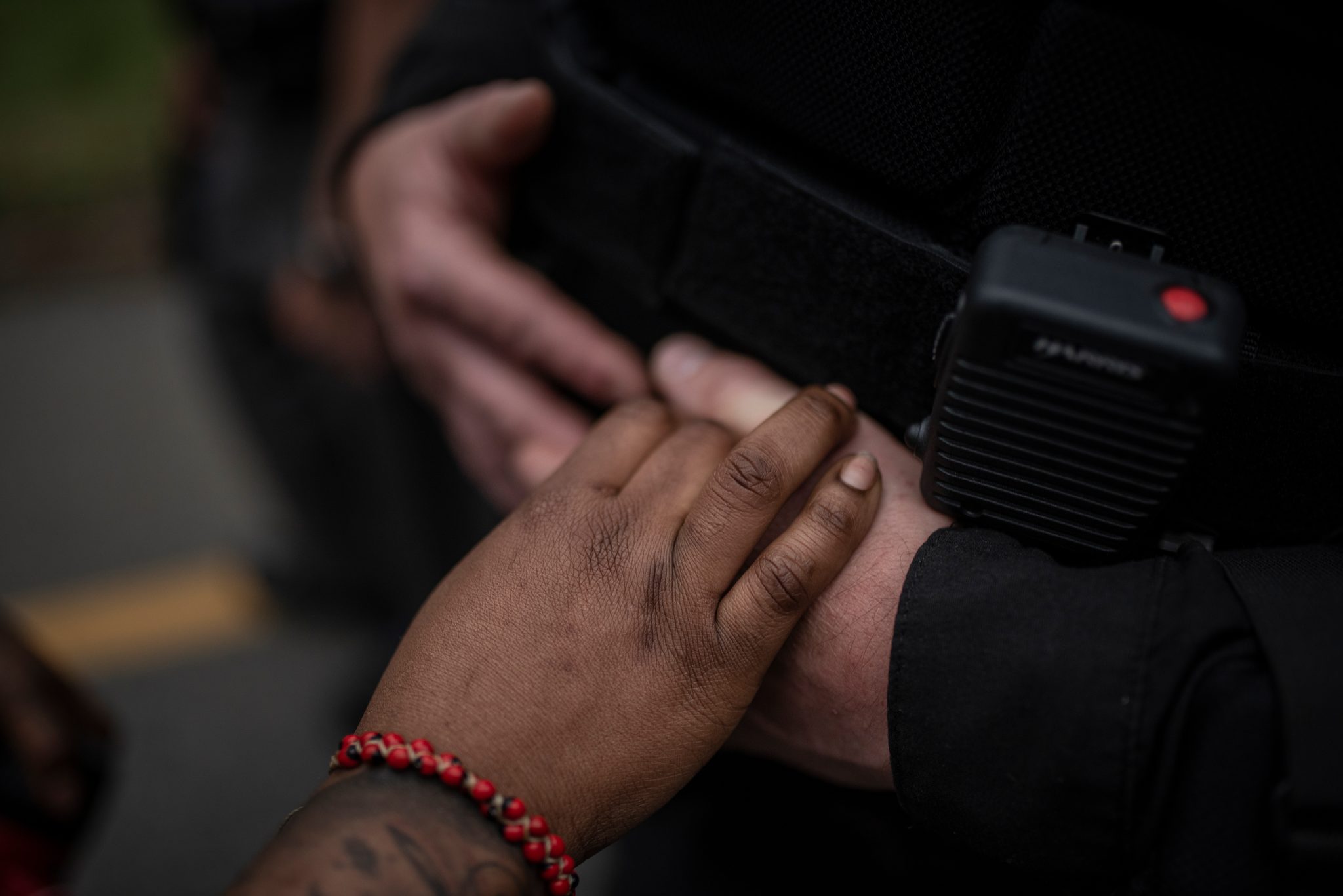 Two hands meet between a red bead bracelet and an officer's radio.