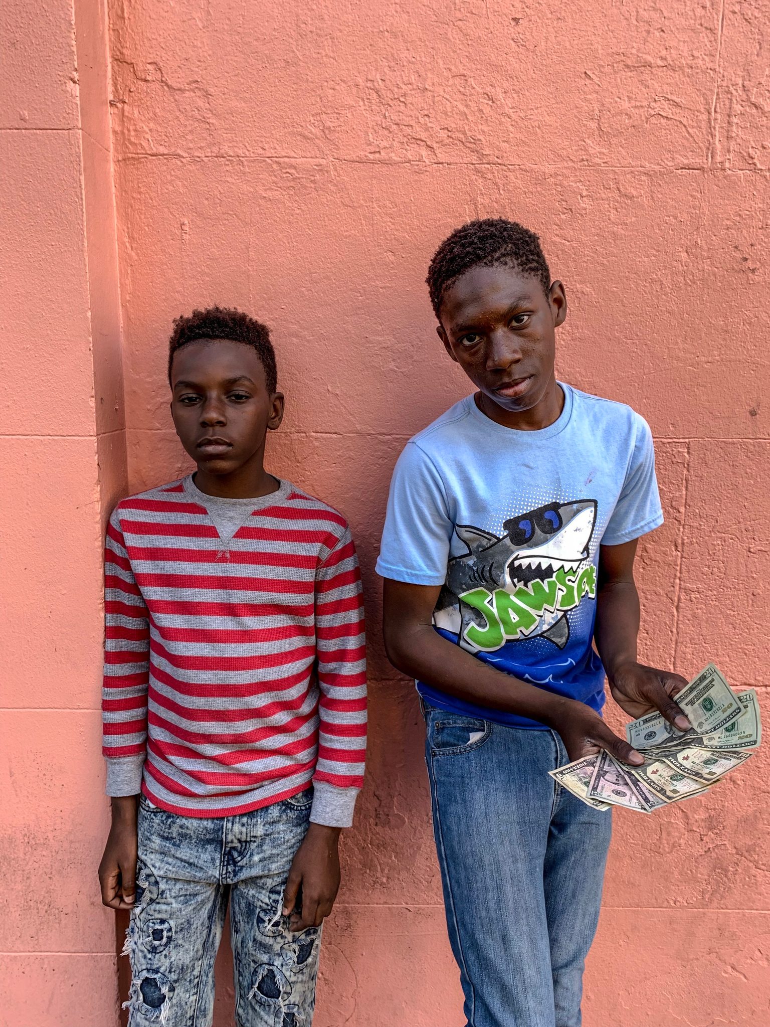 Two boys pose against the salmon wall, one fanning a handful of tip money.