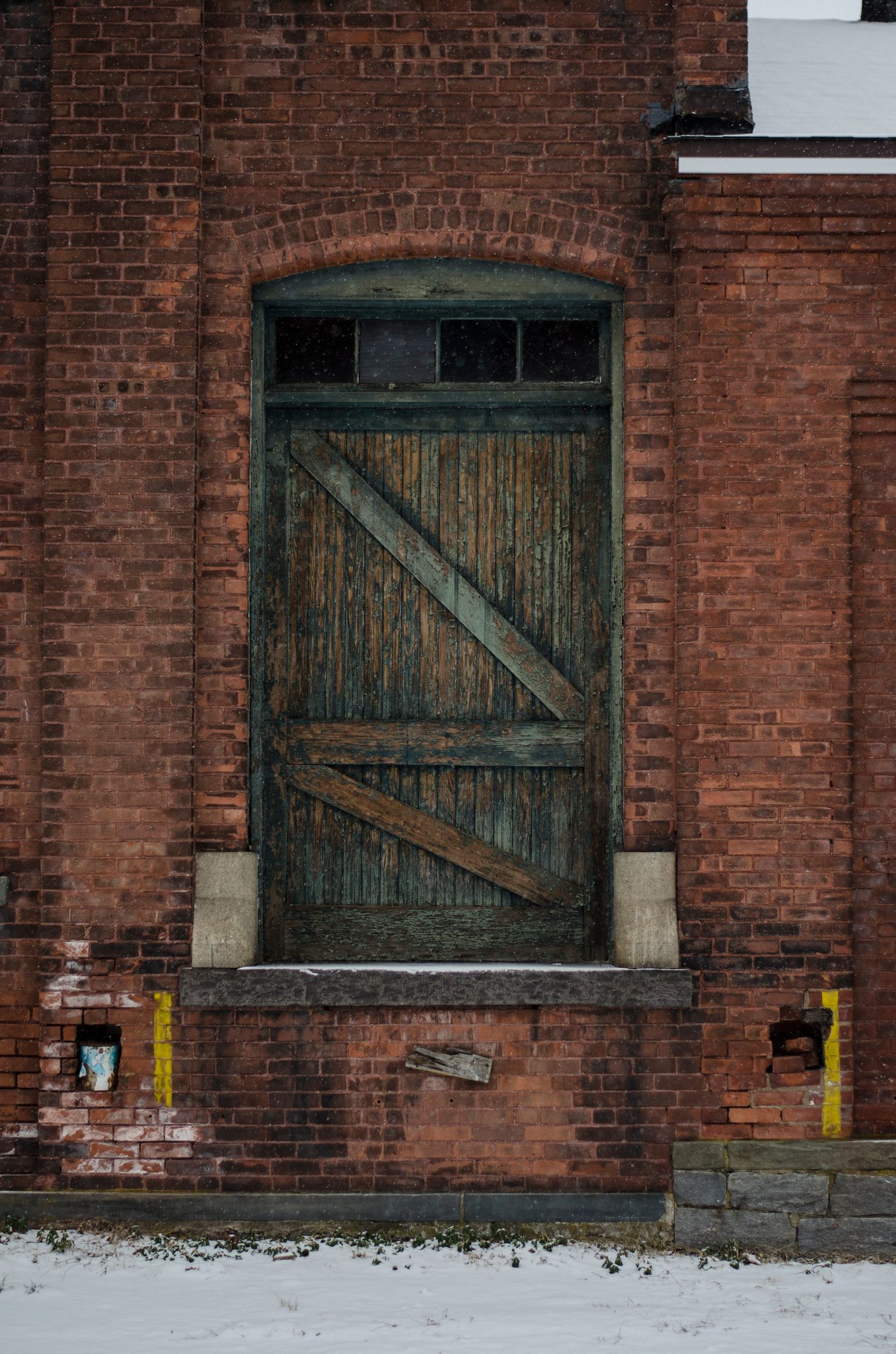 A green barn door set deep in old brick, a dusting of snow at its foot.