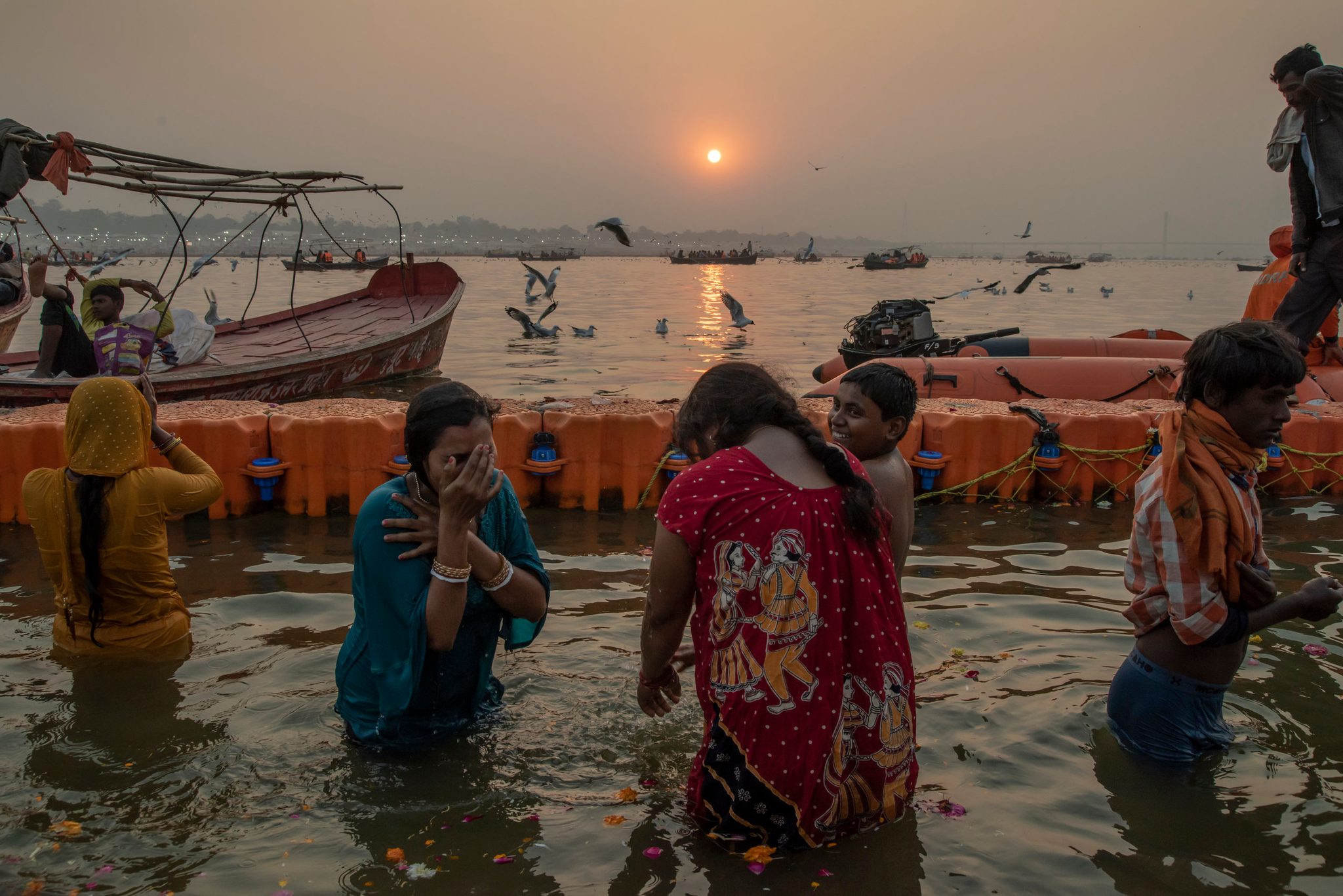 Three young women bathe in the Ganges at sunset.