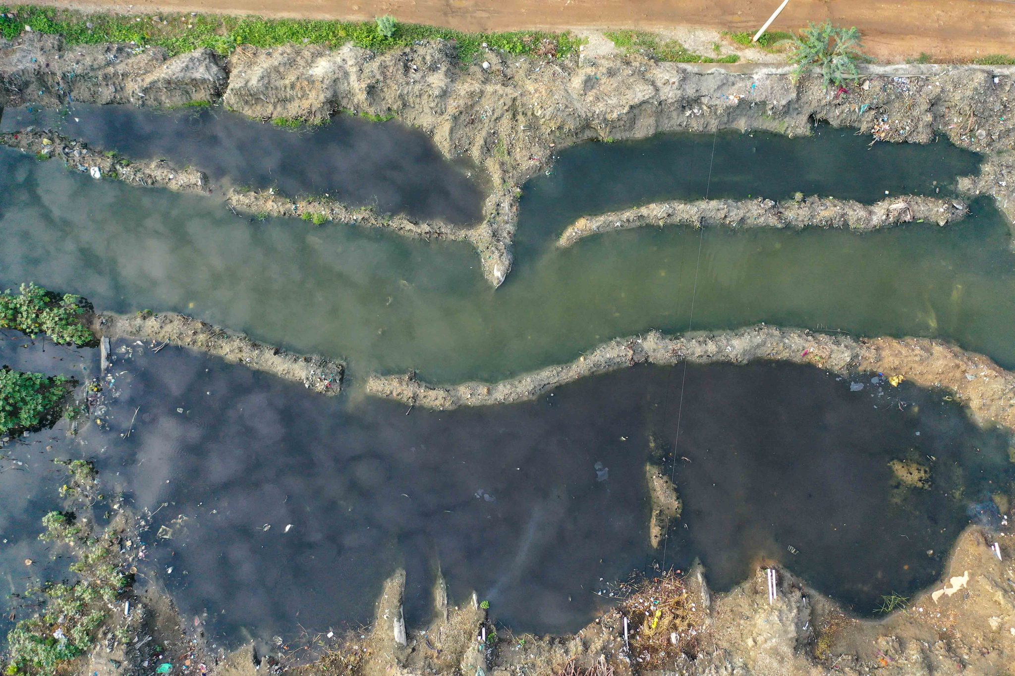 Seen from above, bands of foam and green water pattern the river's edge.
