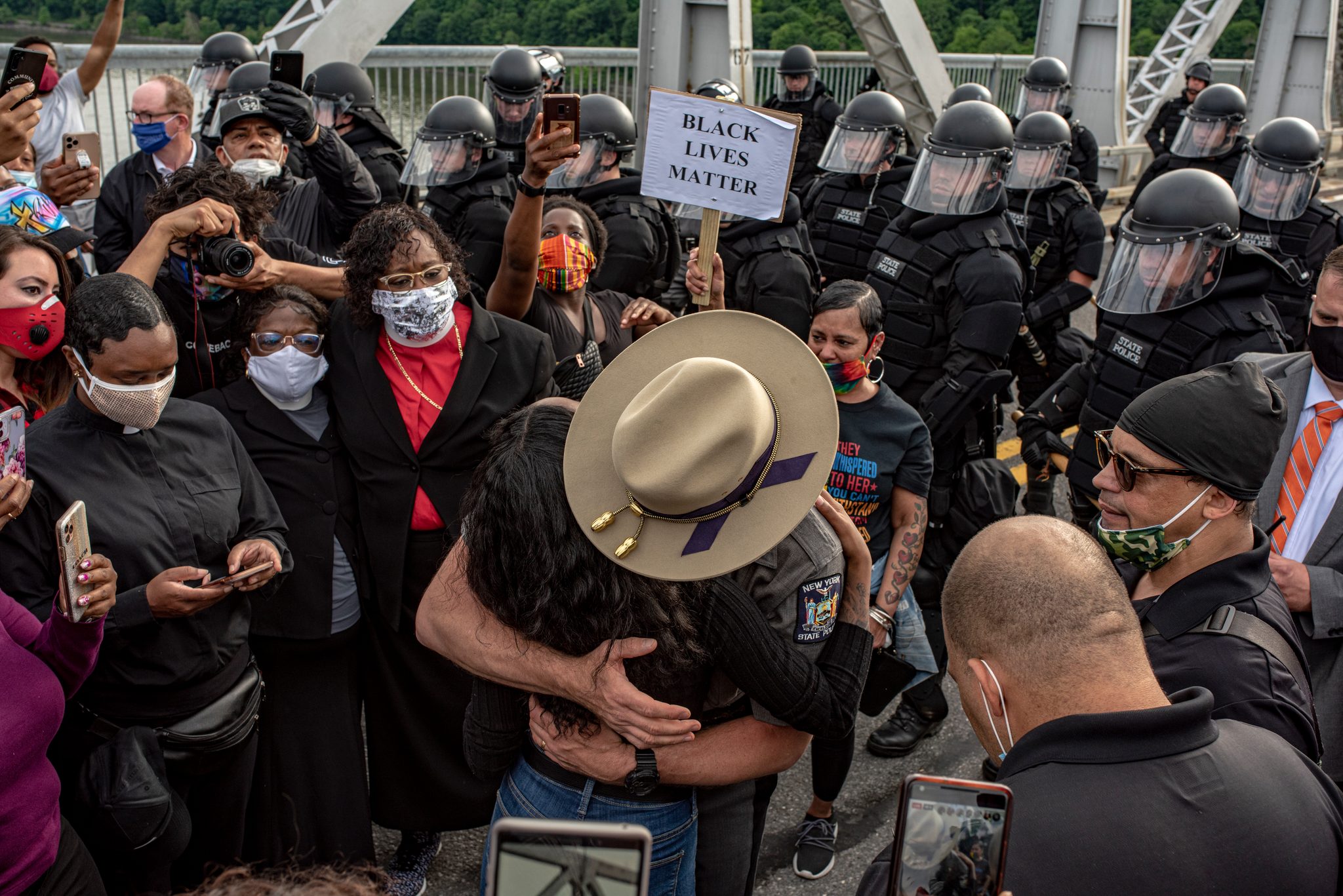 A trooper in a campaign hat pulls a marcher into a hug in front of the riot line.