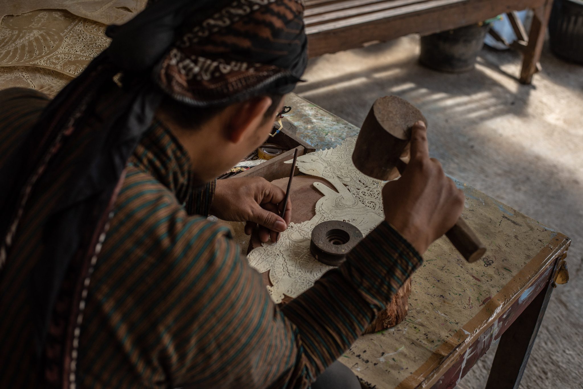 Head bowed under his batik headcloth, he strikes the chisel again and again.