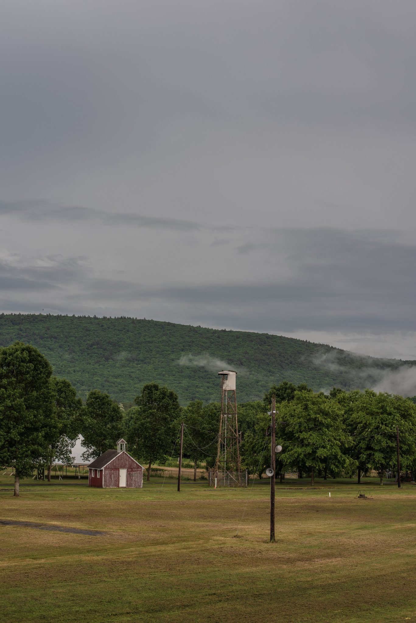 An empty fairground waits under a gray sky, a red shed and a windmill at its edge.