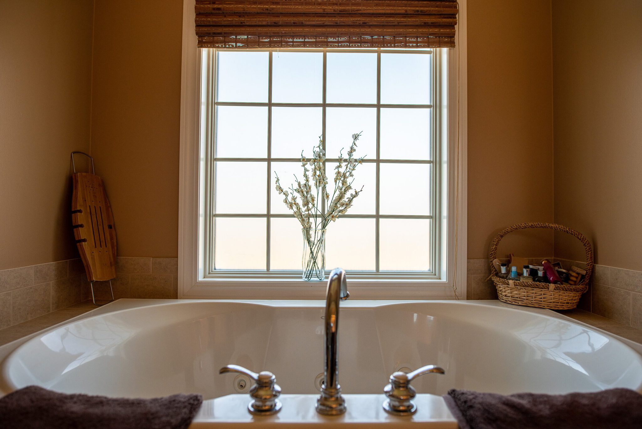 Morning light through a tall window over a deep soaking tub in early April, with a few branches in a glass vase.