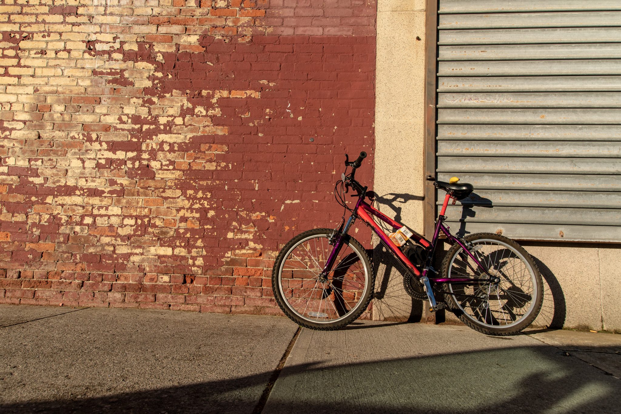 A red bike leans against a weathered brick wall in the late sun.