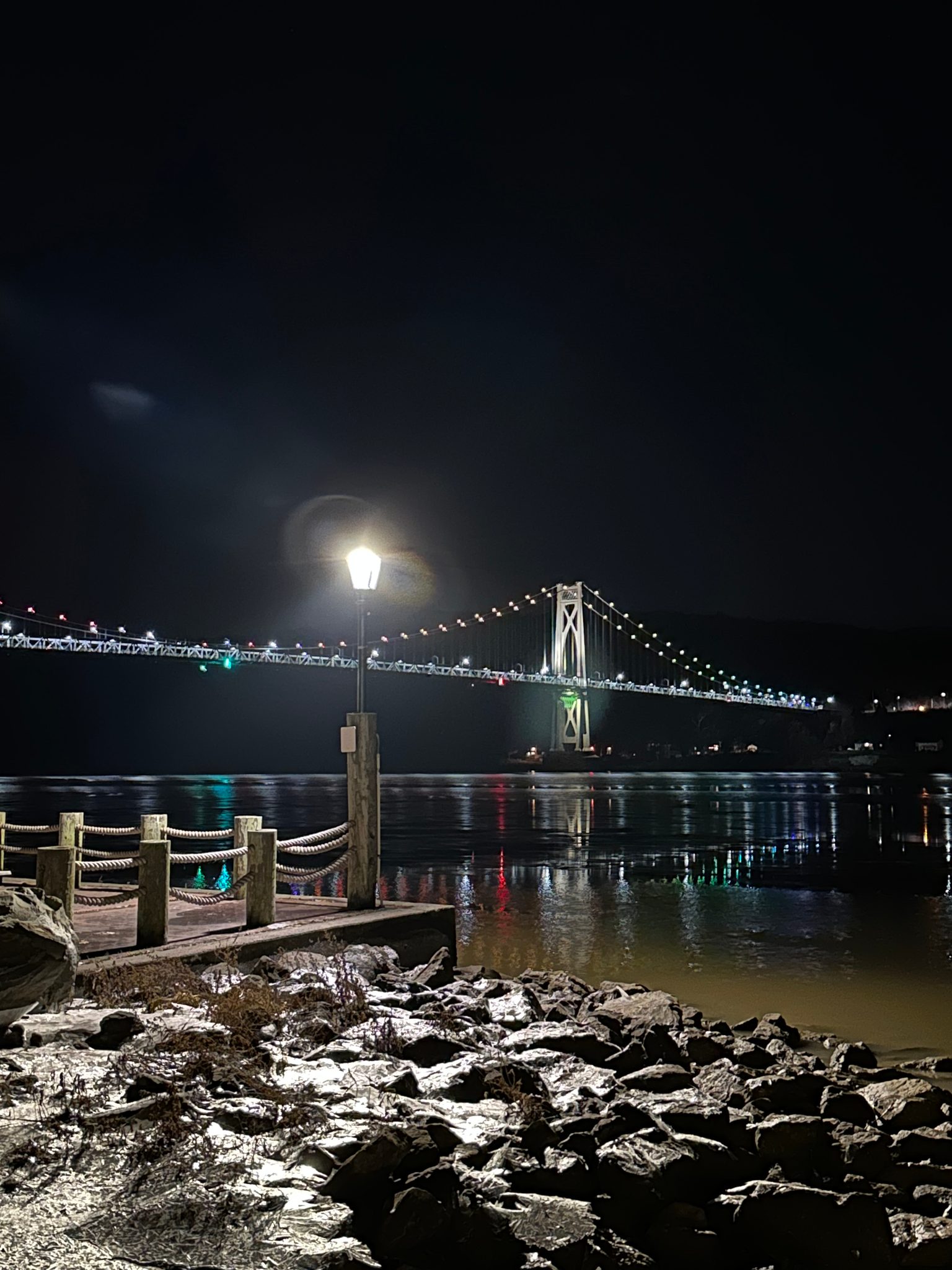 A lamp post and icy rocks before the bridge at night.
