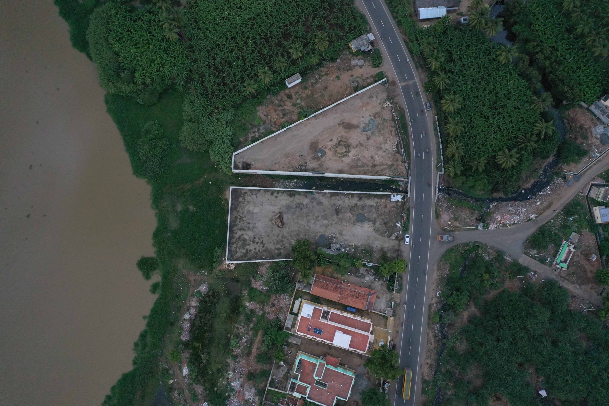 A road runs along the river past walled plots and red roofs.