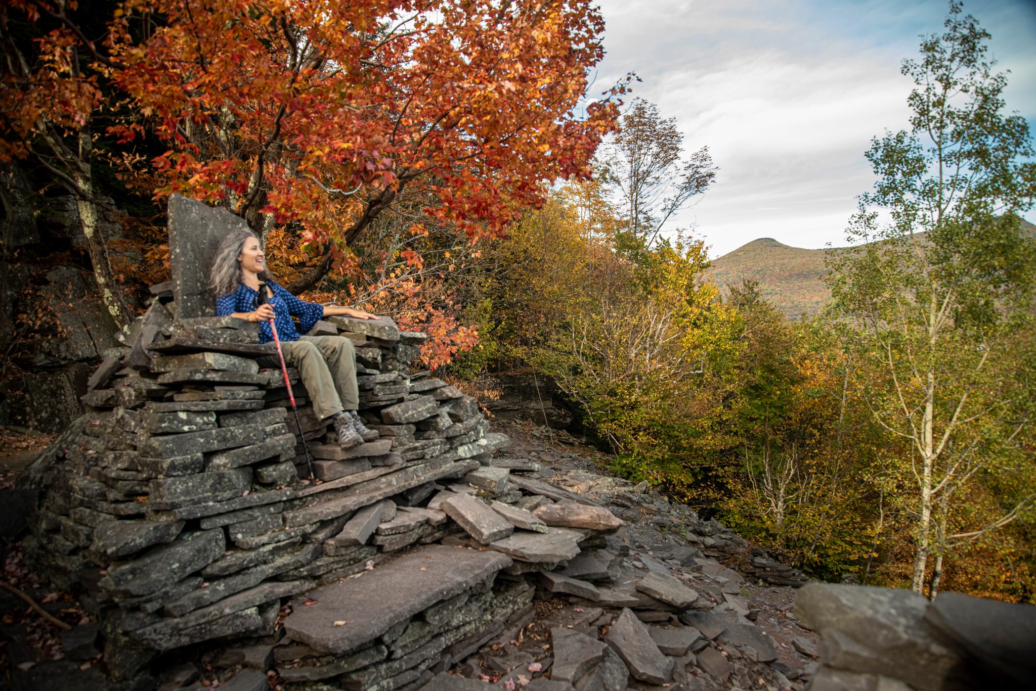 A hiker rests on a throne of stacked slate, the maples burning red around her.
