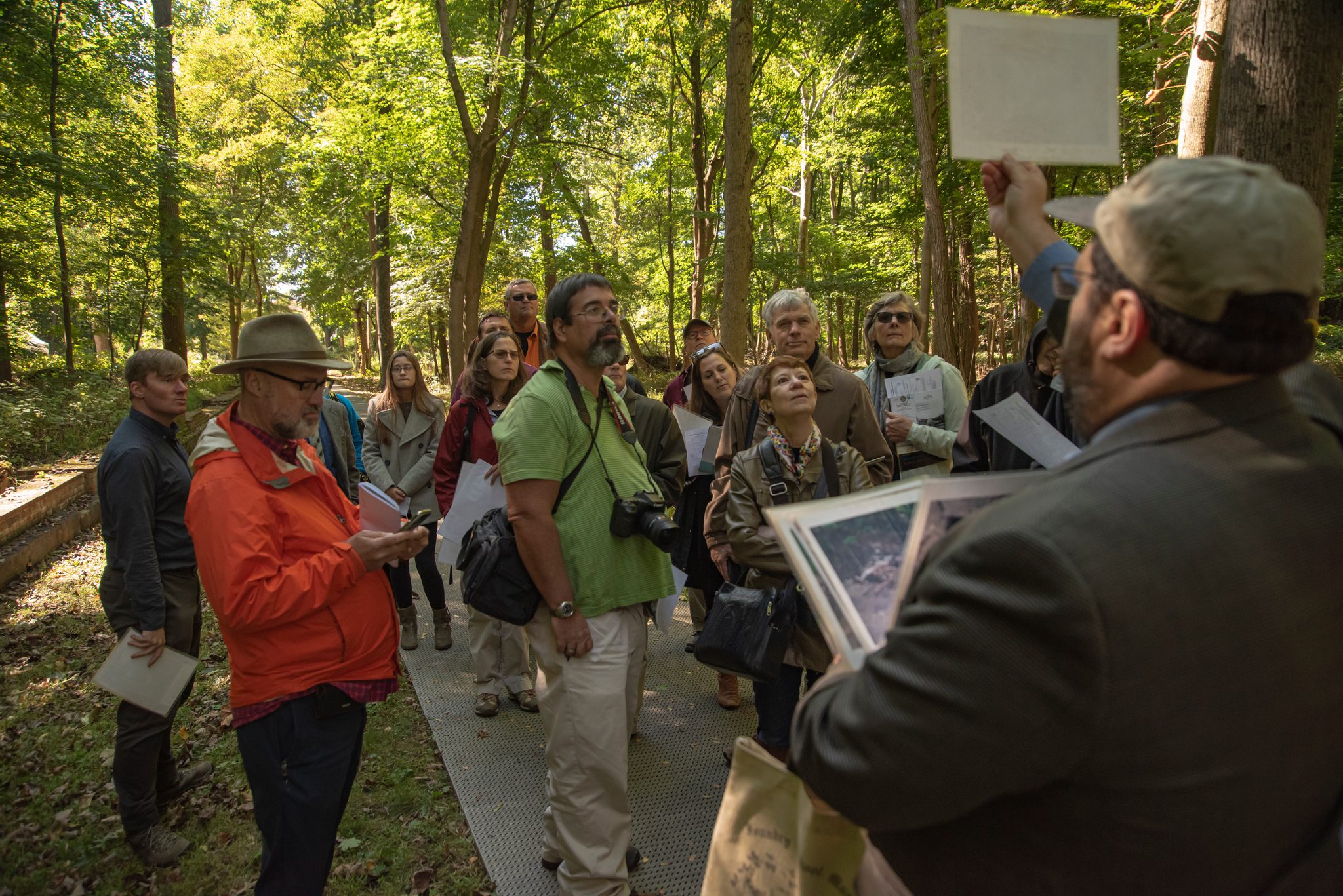 A guide holds up an old photograph so the group can see what once stood among these trees.