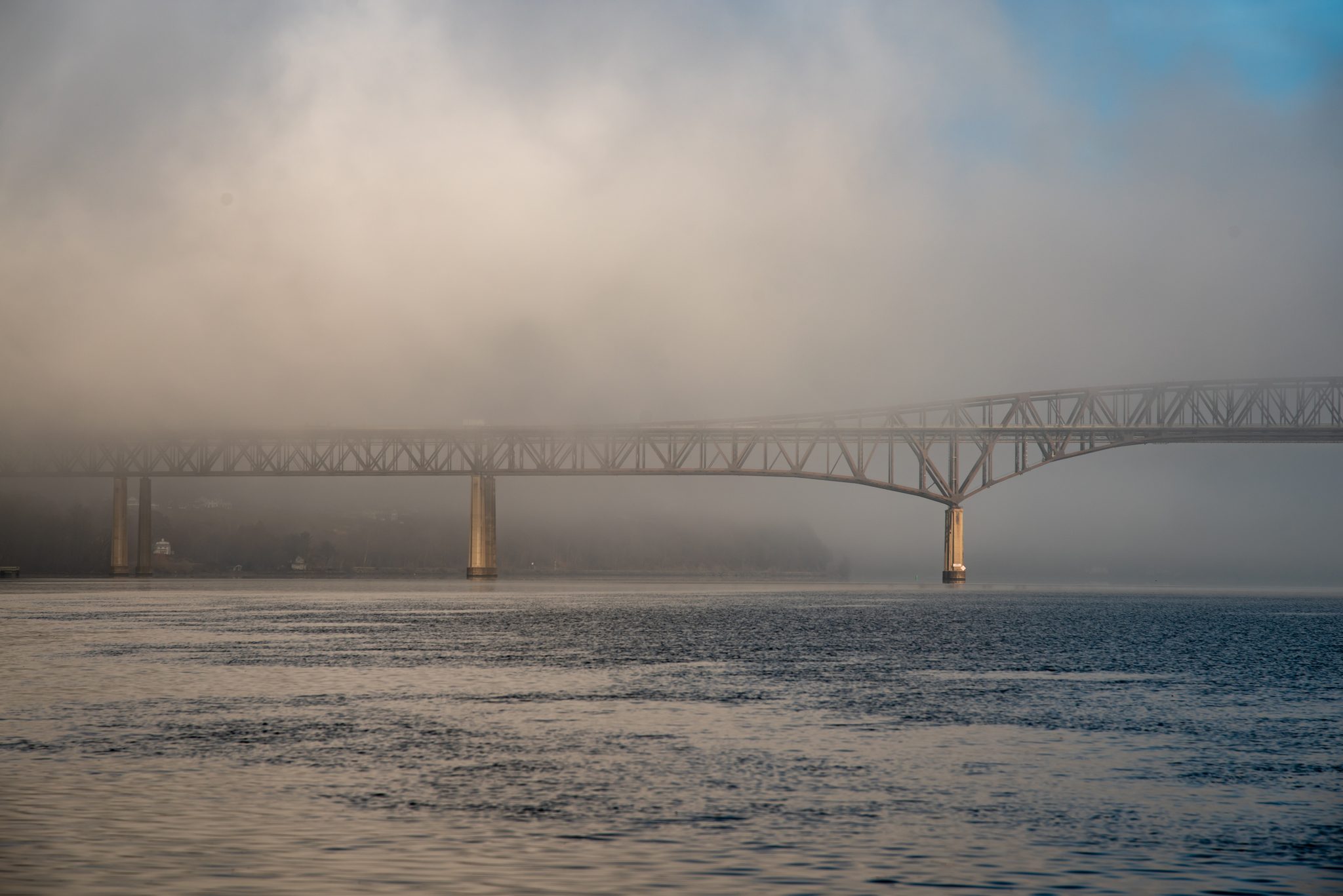 A long bridge laid low across the river in morning fog.