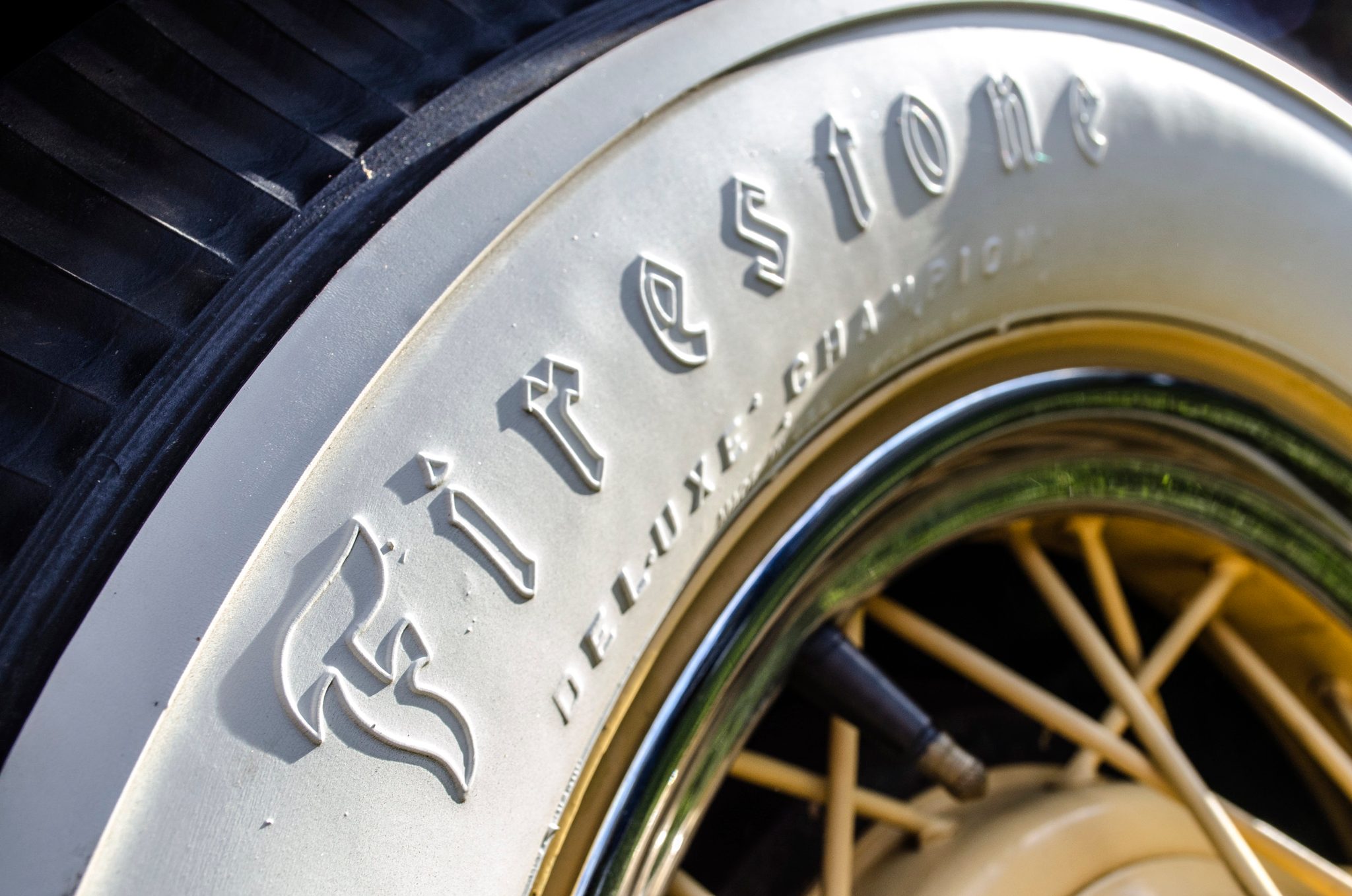 A whitewall tire on an old car, Firestone Deluxe Champion raised on the rubber.