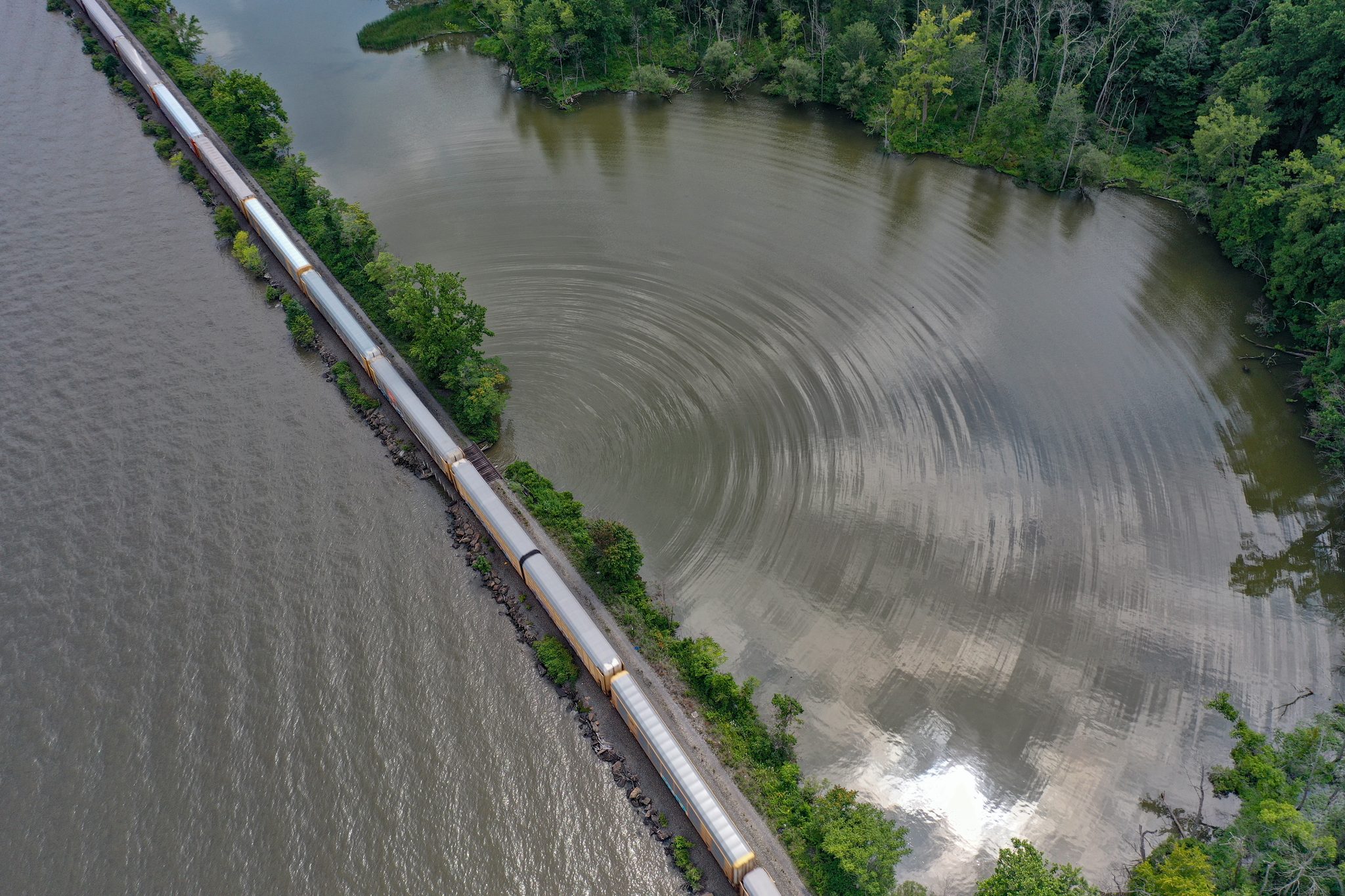 A freight train threads the causeway between the river and a still cove.