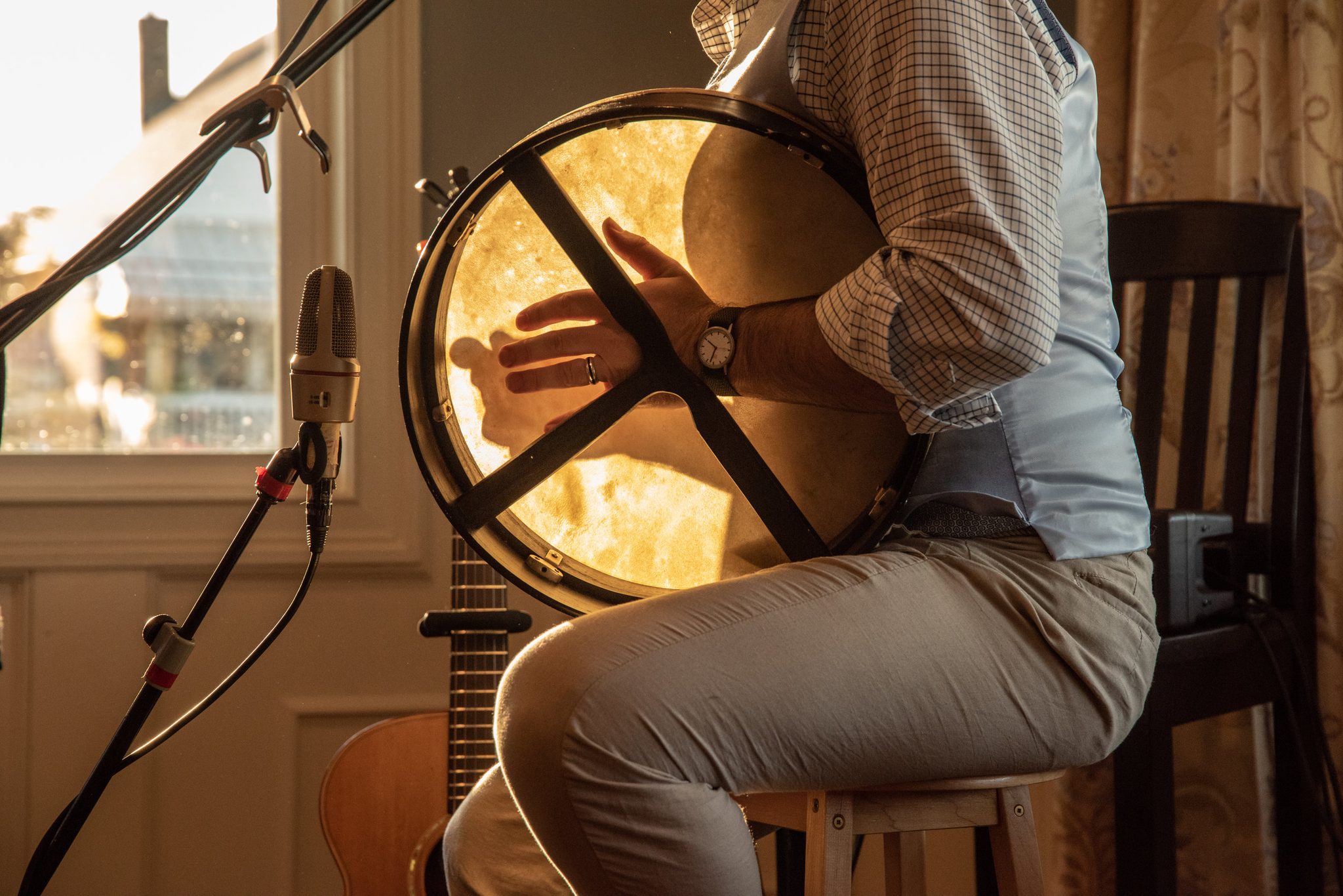 Emmet trades the guitar for the bodhrán, the drumhead glowing in the window light.