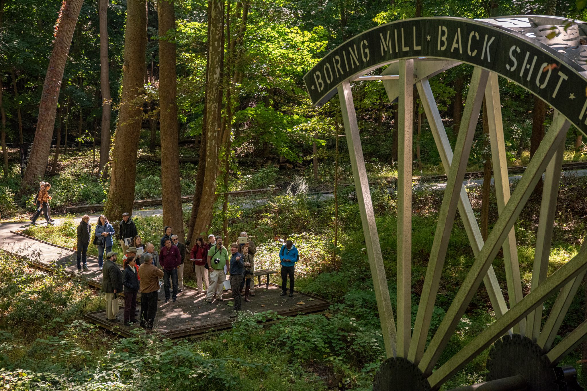 Visitors gather on the boardwalk beneath a steel outline of the boring mill's back shot wheel.